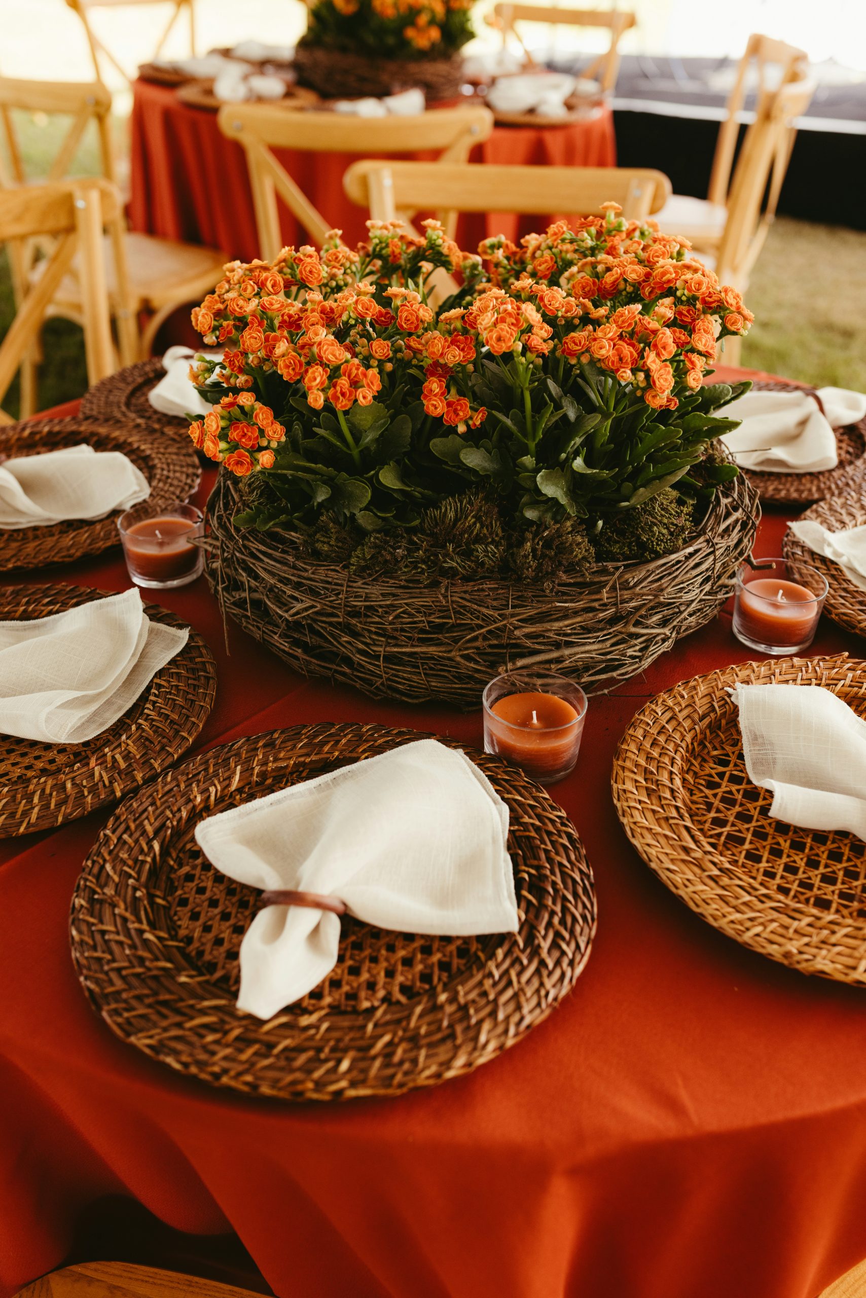 Table set with orange flowers, red tablecloth, and woven placemats.