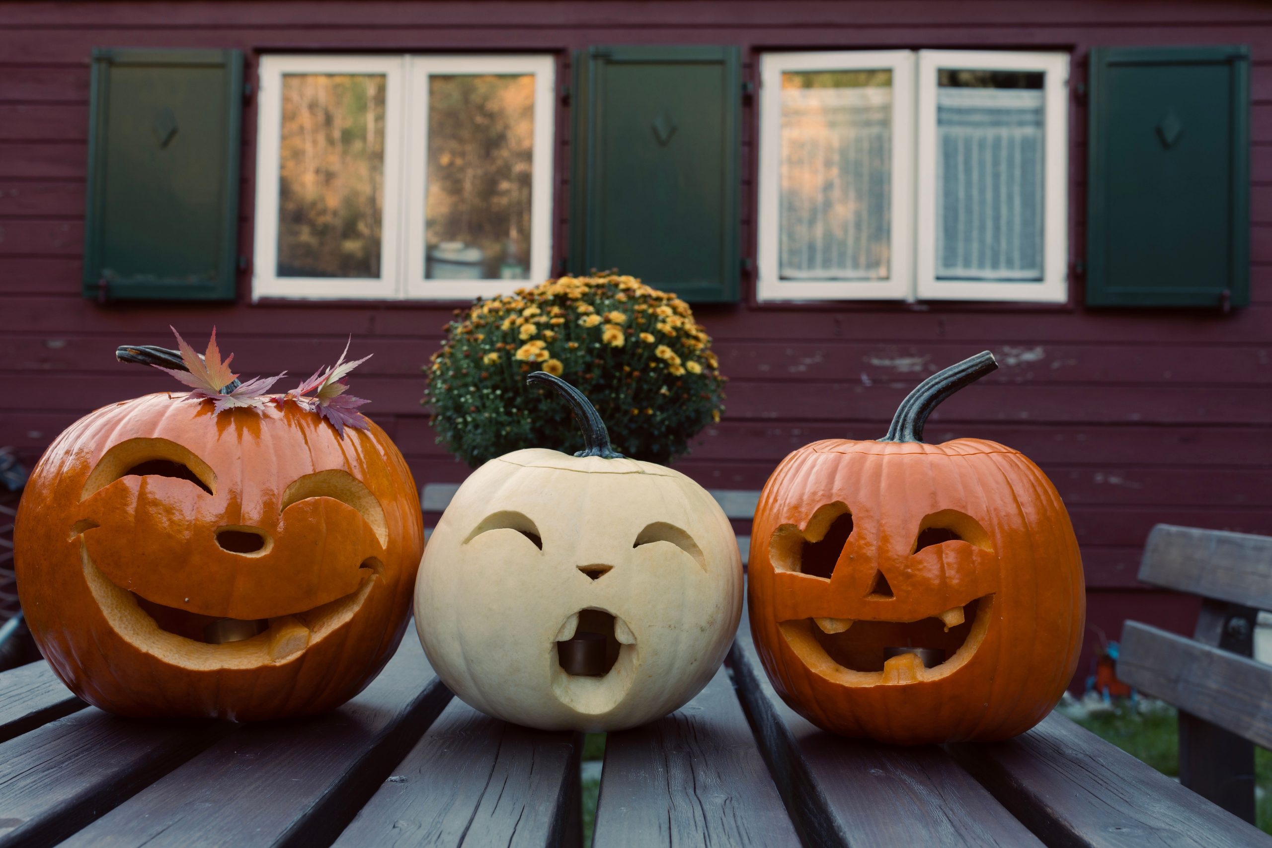 Three carved pumpkins with funny expressions adorn a wooden table, celebrating Halloween outdoors.