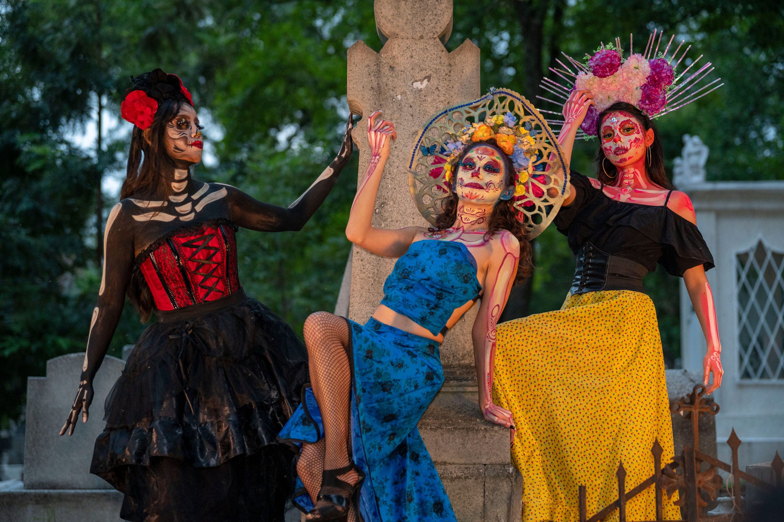 Three women in traditional Dia de los Muertos attire with painted faces celebrate the cultural festival.