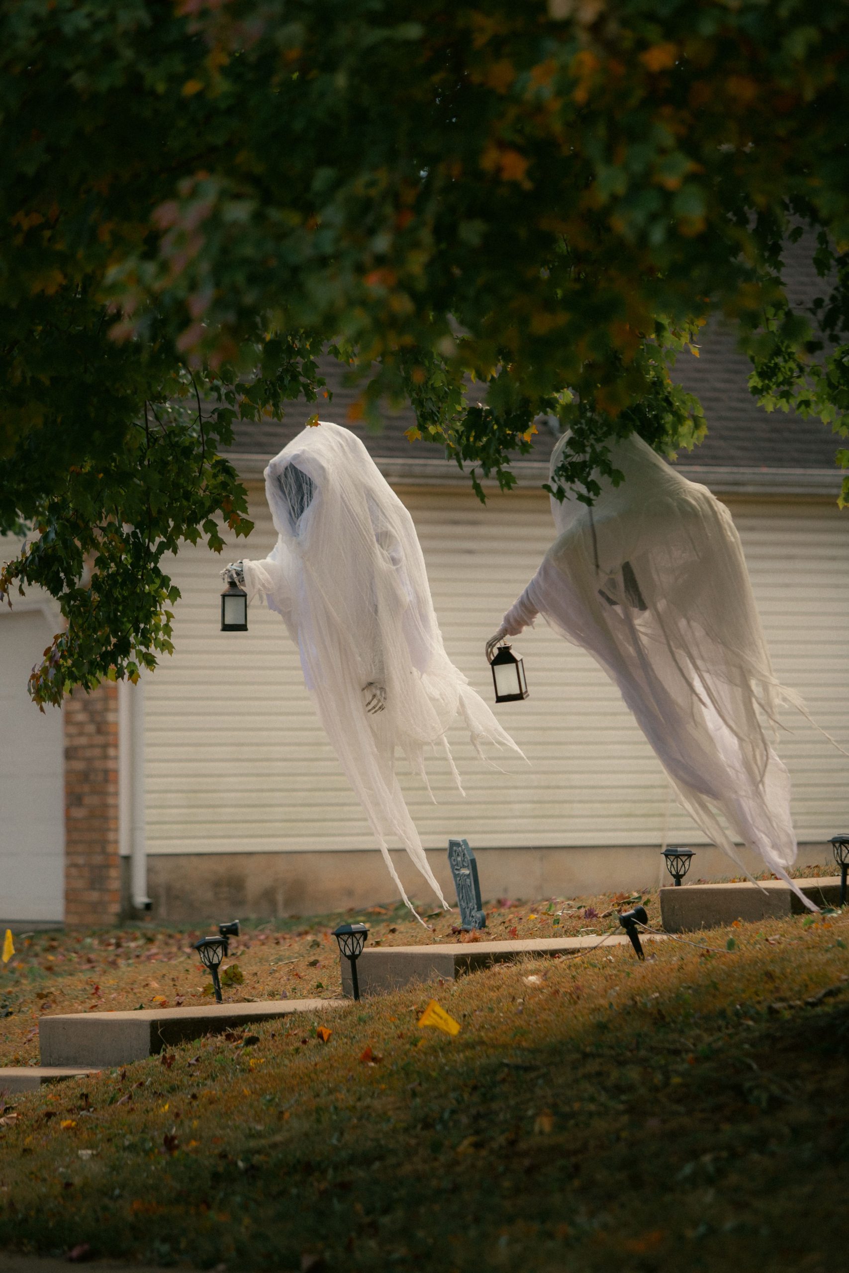 Two ghost figures hanging from trees in a garden, creating a spooky Halloween scene.