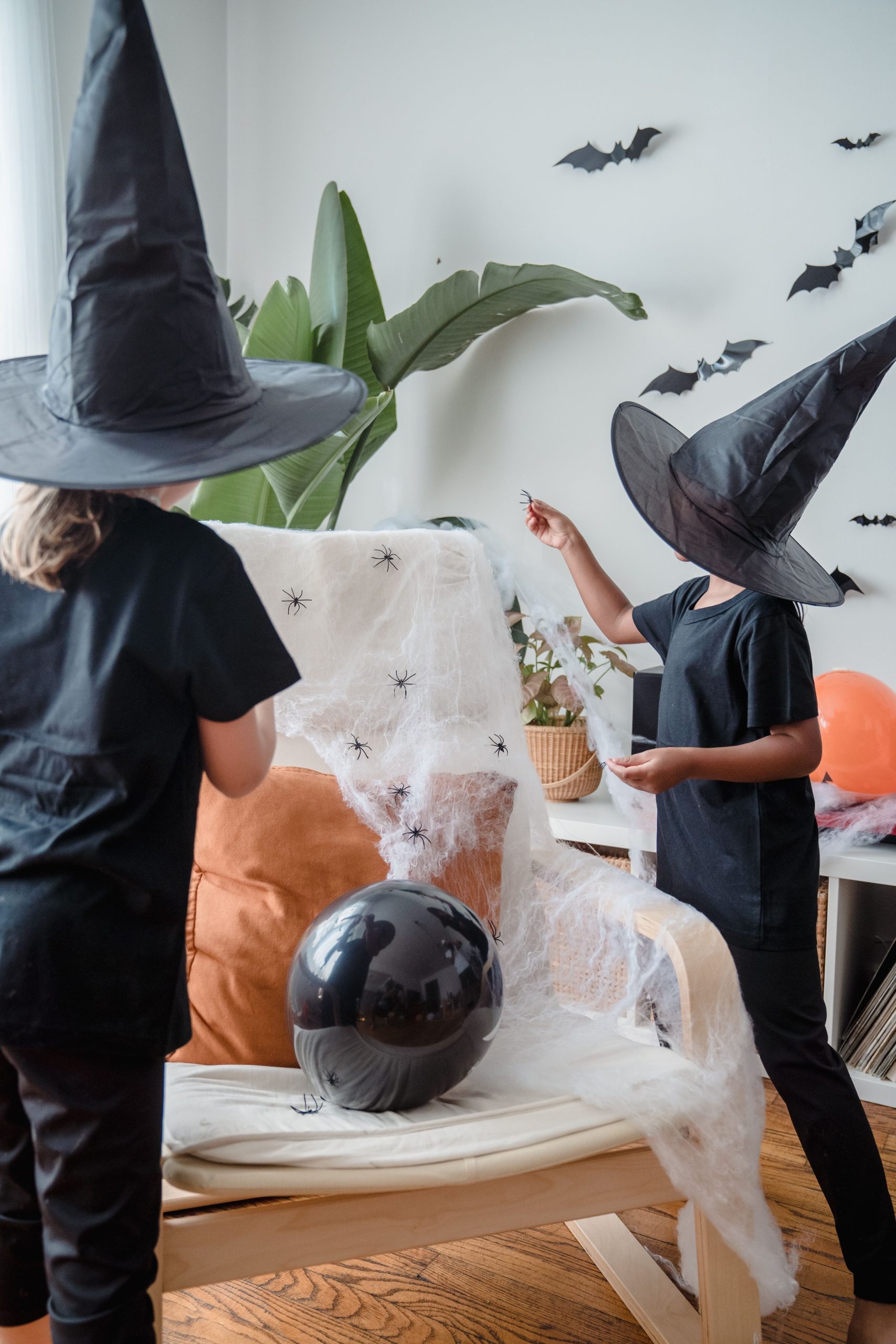 Two kids in witch costumes decorate for Halloween indoors, creating a spooky atmosphere.