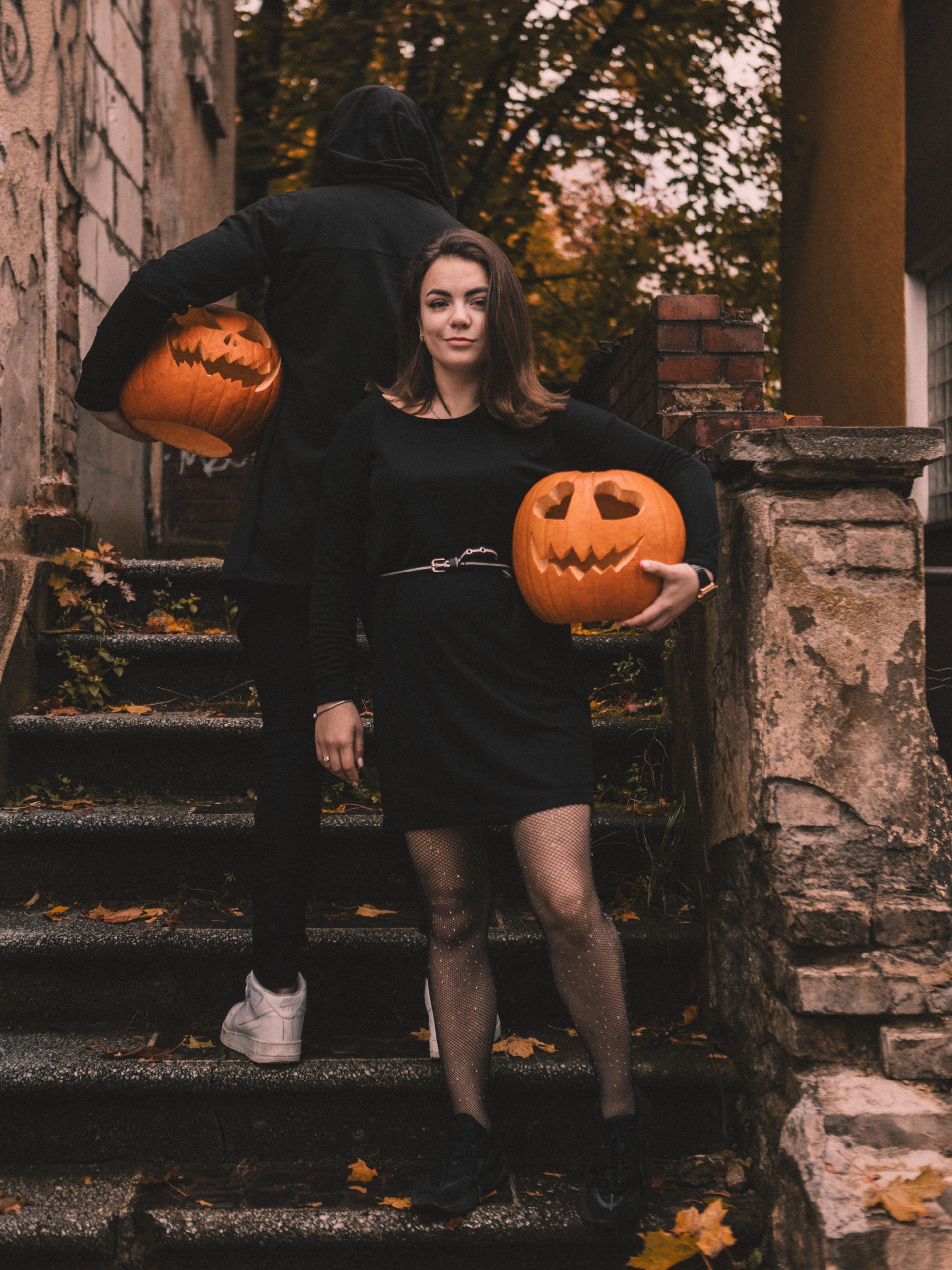 Two people posing with carved pumpkins on a staircase during autumn.