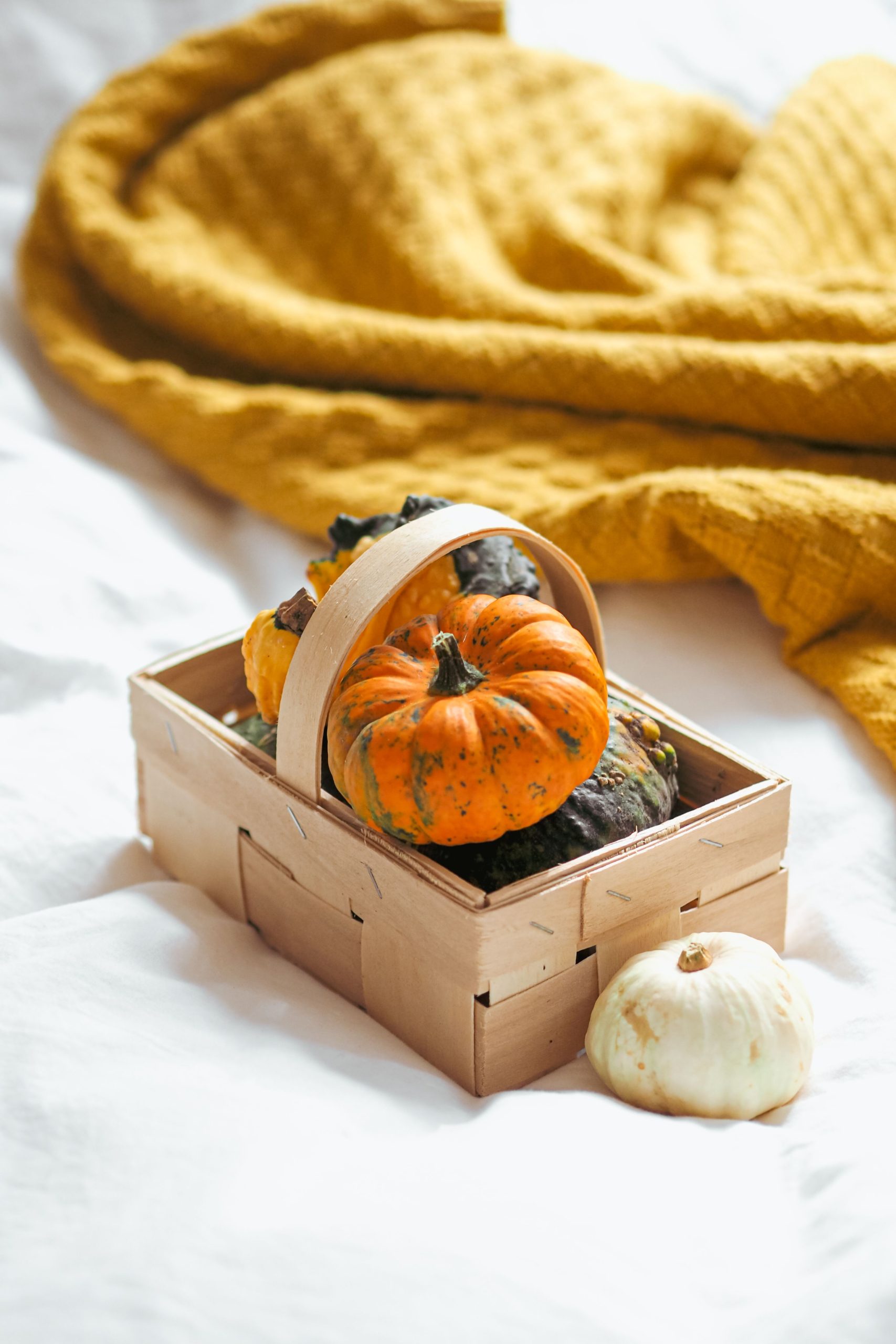 Vibrant pumpkins in a wooden basket against a cozy fall background.