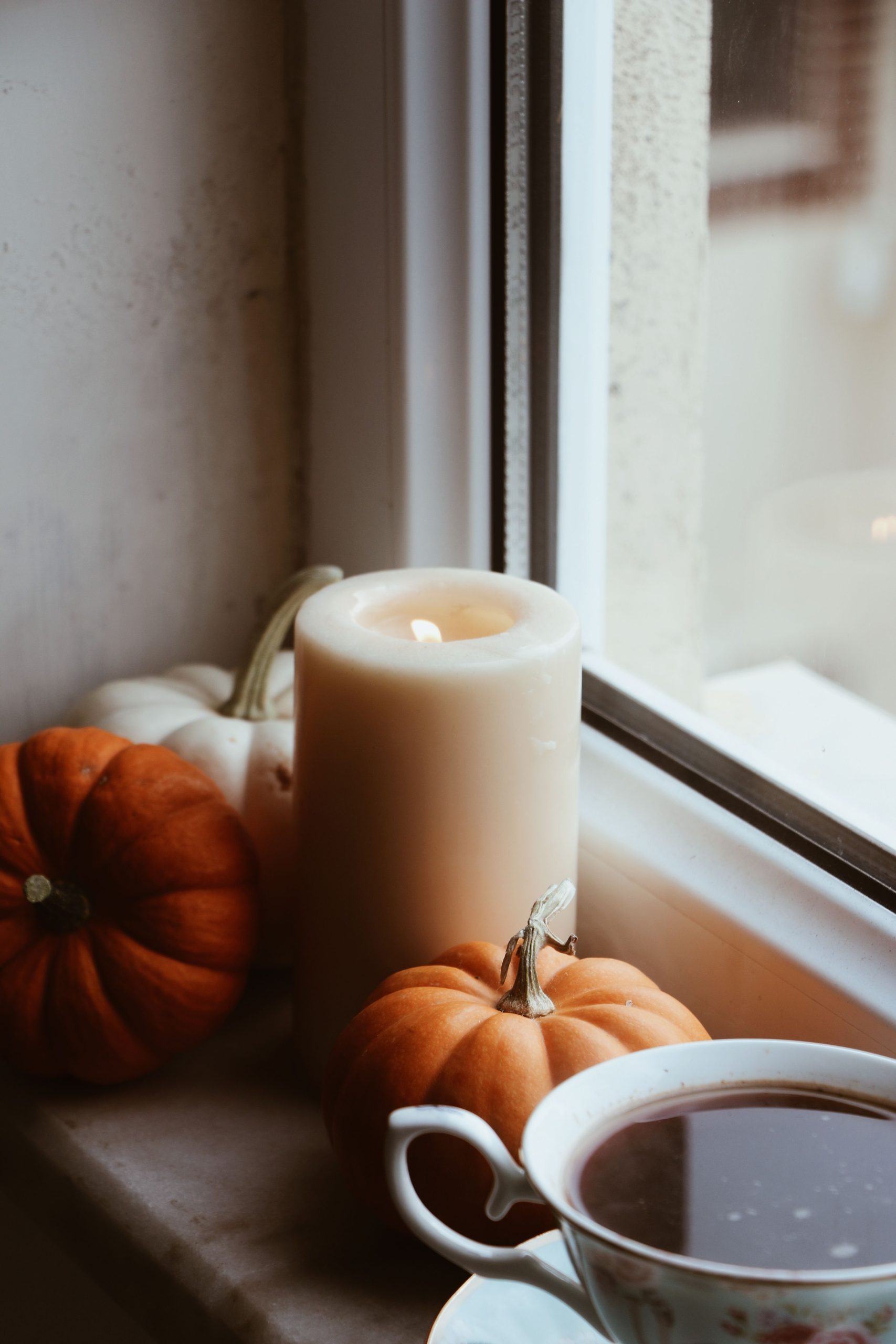 Warm and inviting autumn scene with pumpkins, candle, and tea by the window.