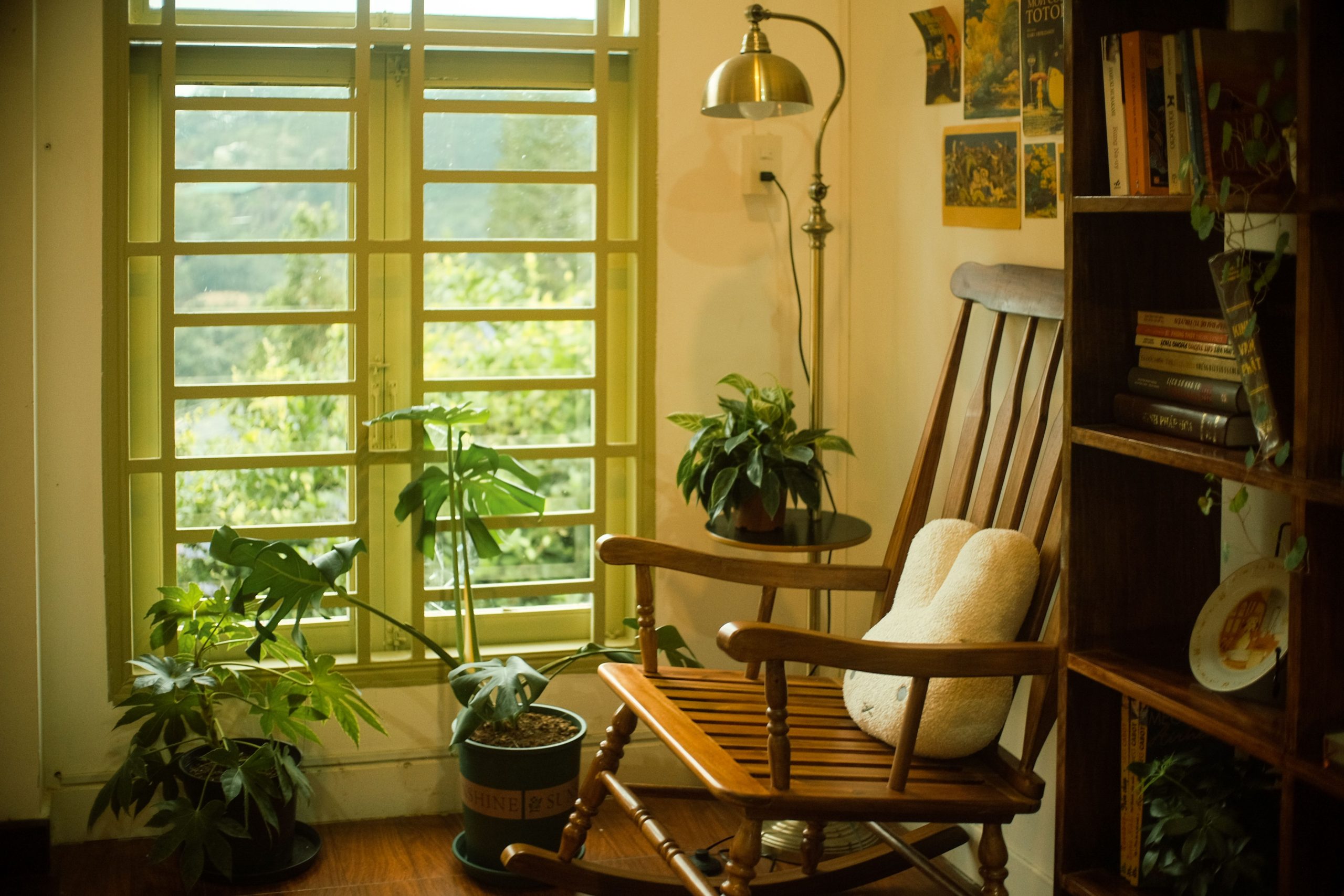 Warm and inviting reading nook with a wooden rocking chair, plants, and books by a window.