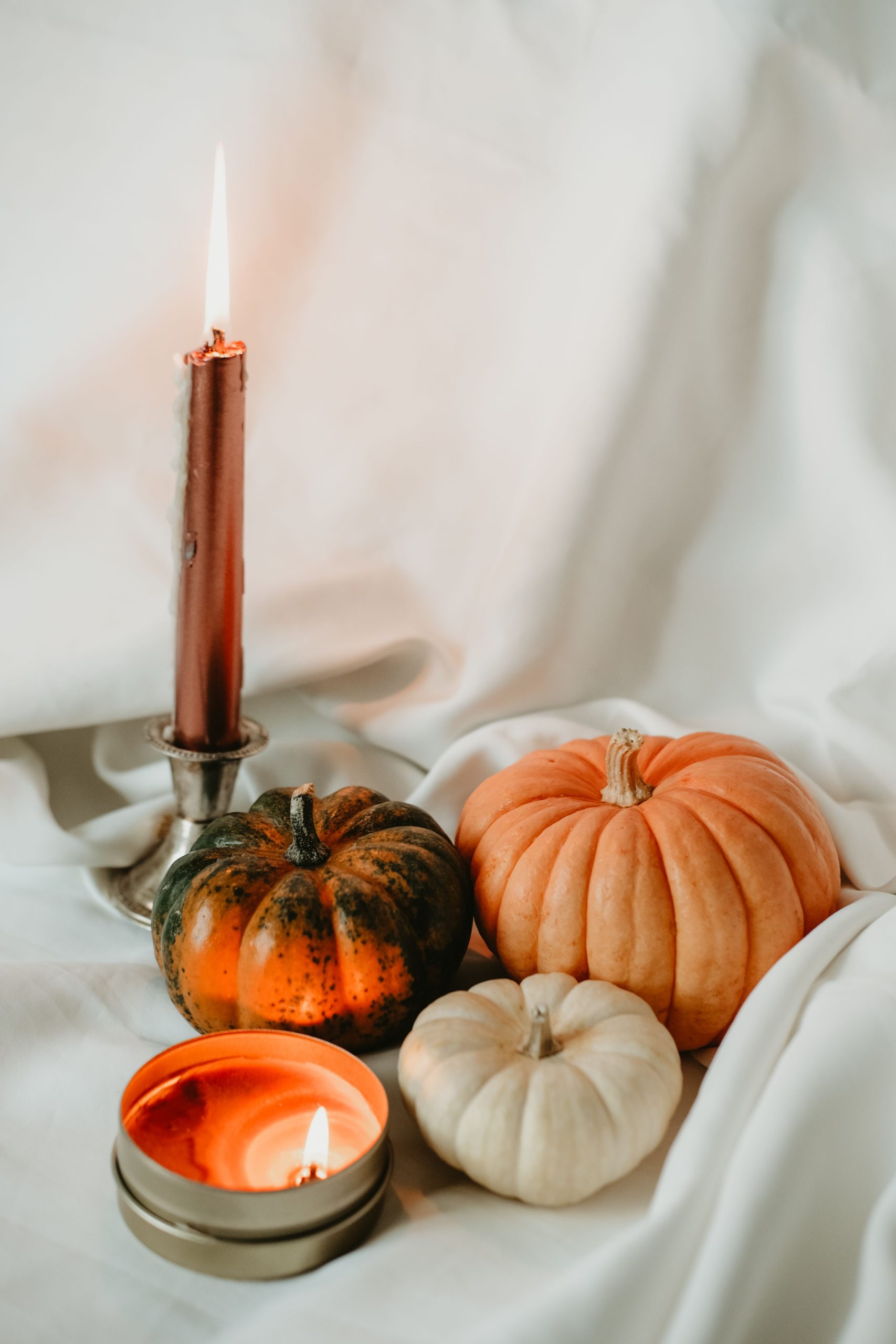 Warm autumn ambiance featuring candles and pumpkins on soft fabric backdrop.