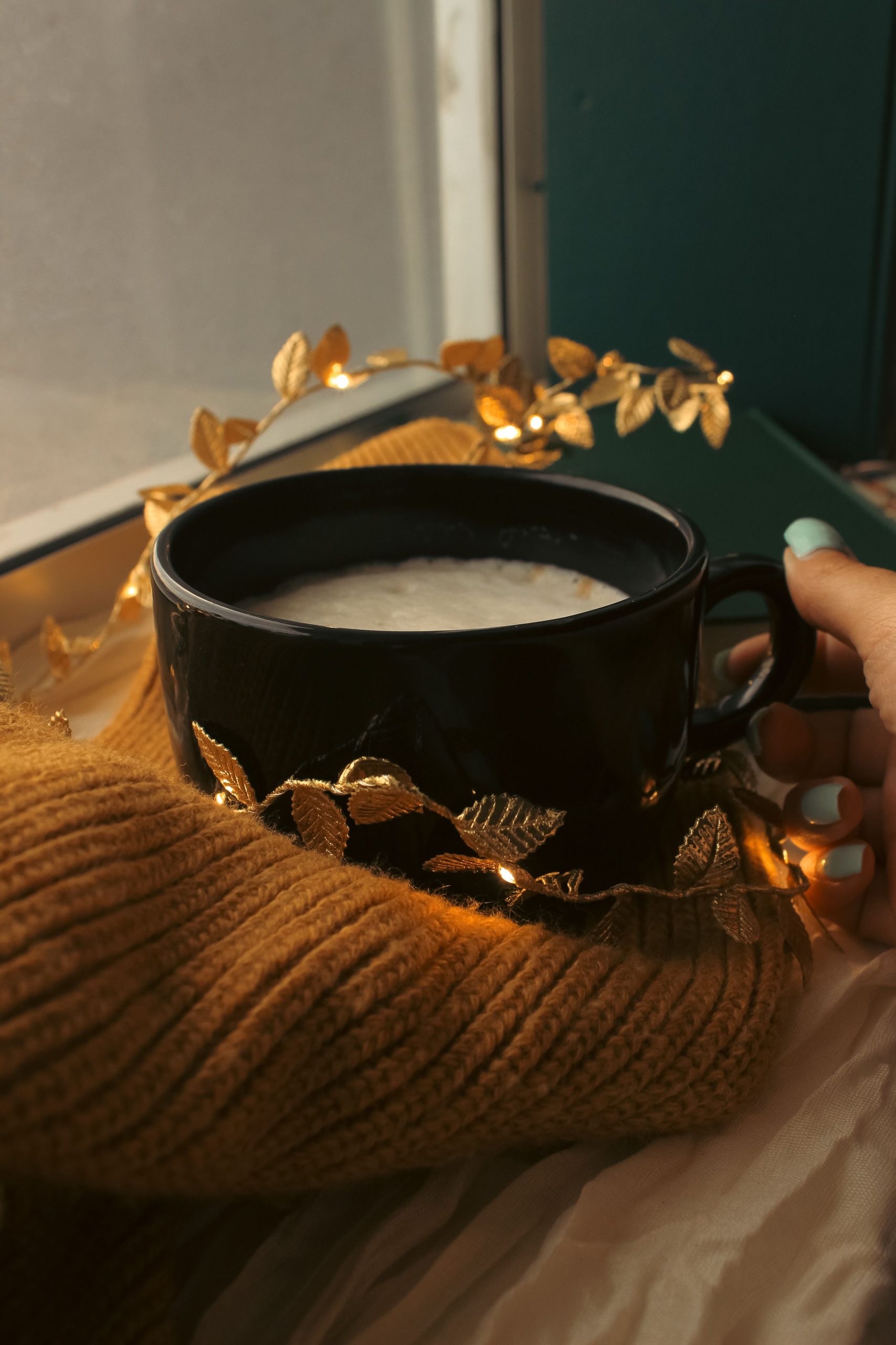 Warm autumn atmosphere with coffee cup, golden leaves, and cozy sweater by the window.