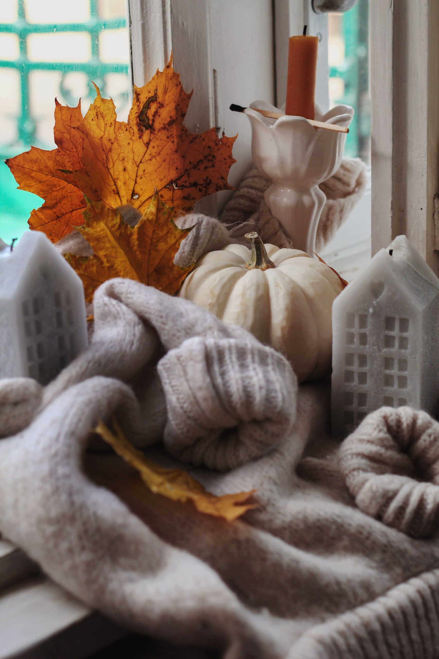 Warm autumn scene with candles, leaves, and pumpkins on a cozy windowsill.