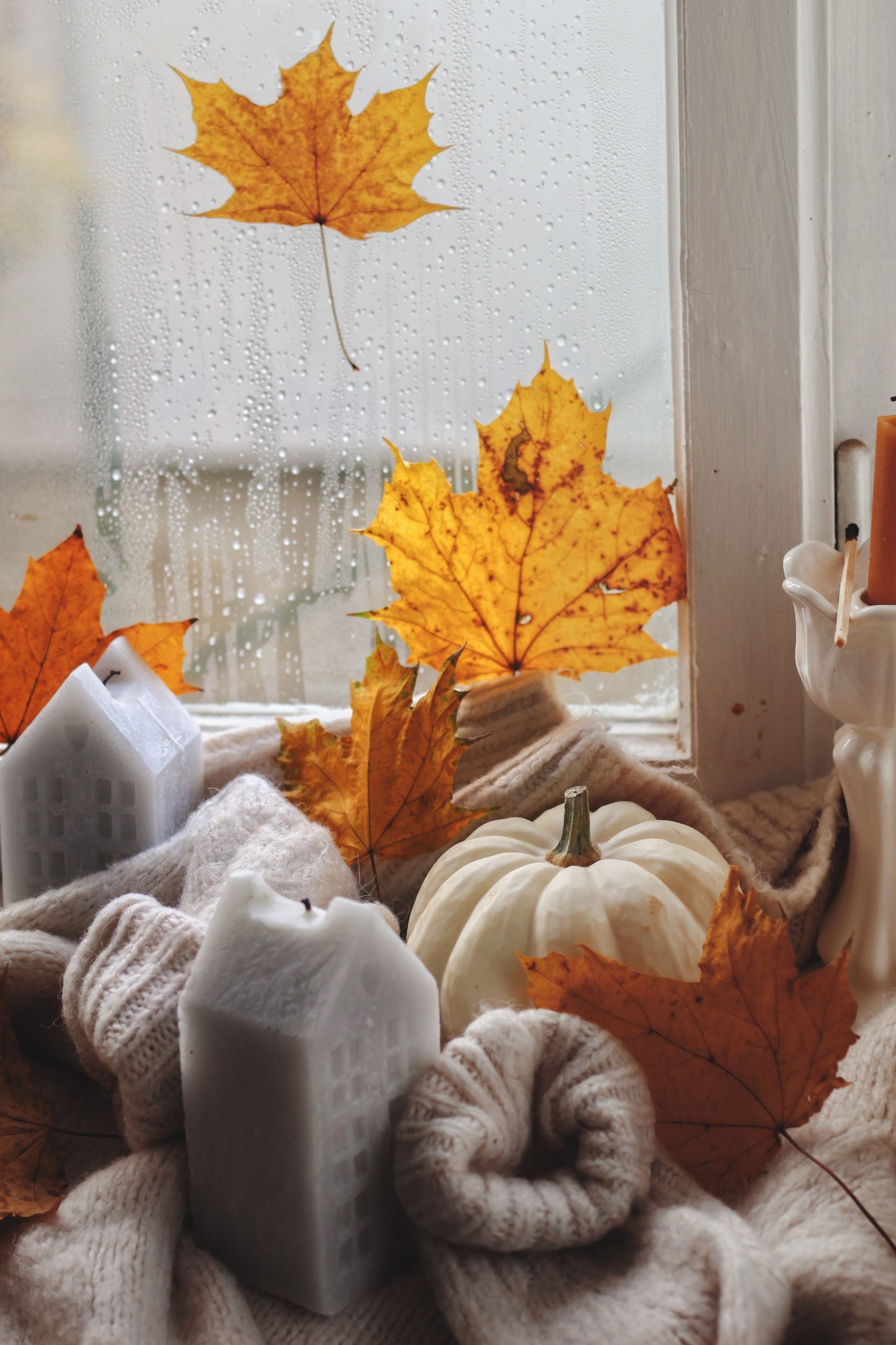 Warm autumn scene with candles, leaves, and pumpkin on a windowsill.