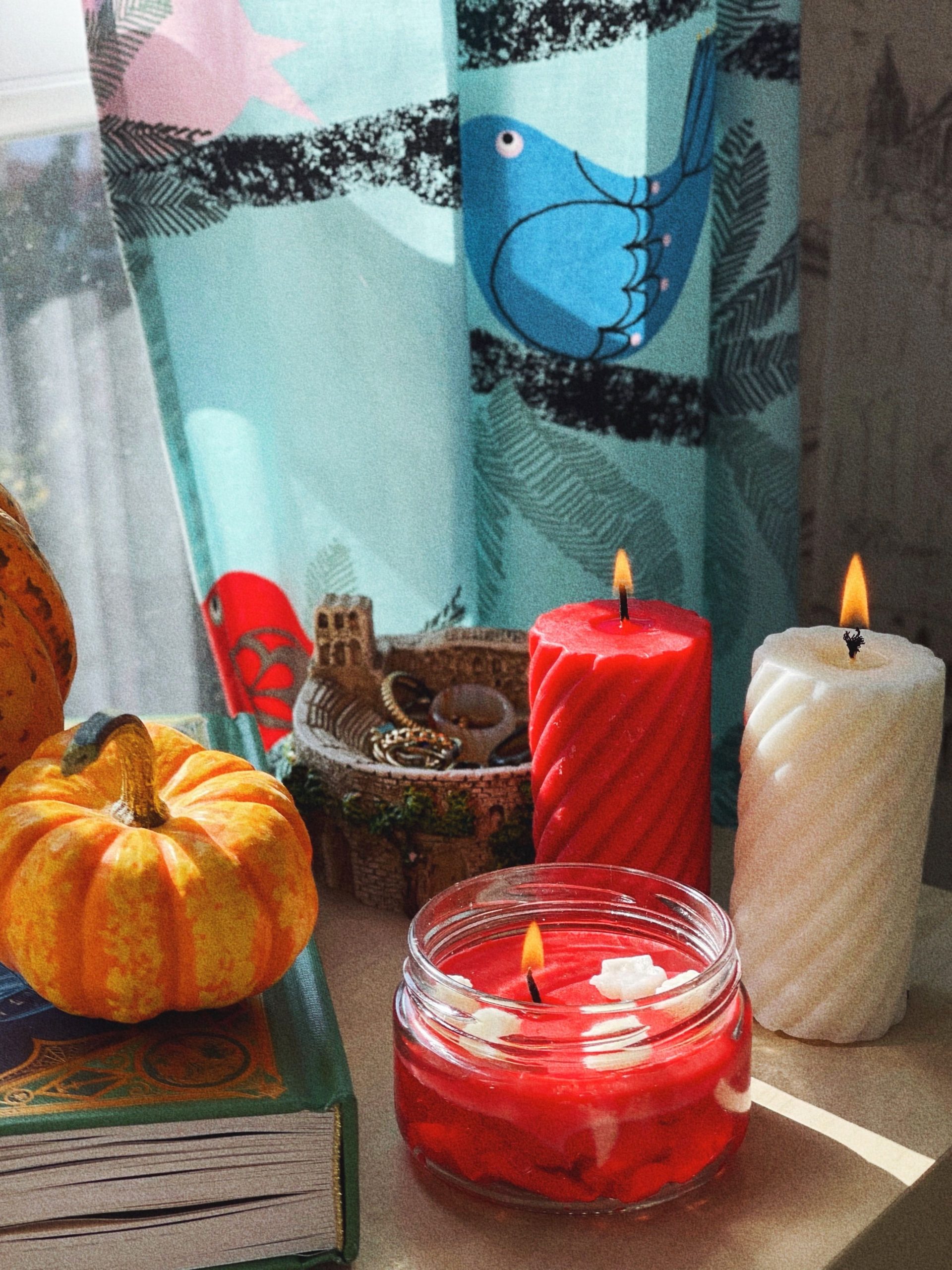 Warm autumn setting with candles, a pumpkin, and decorative elements by a window.
