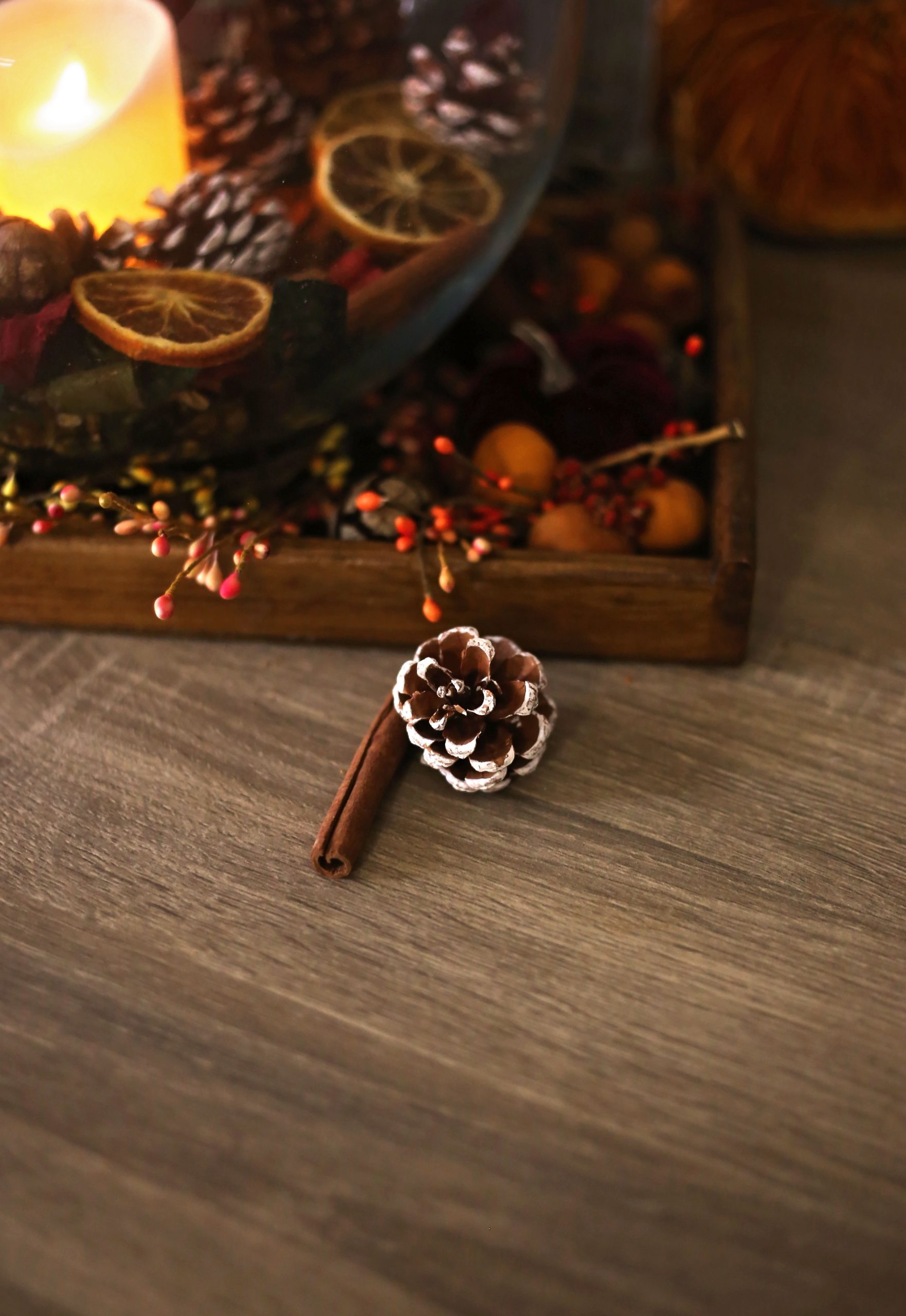 Warm autumn setting with candles, pine cones, and cinnamon on a wooden surface creates a cozy atmosphere.