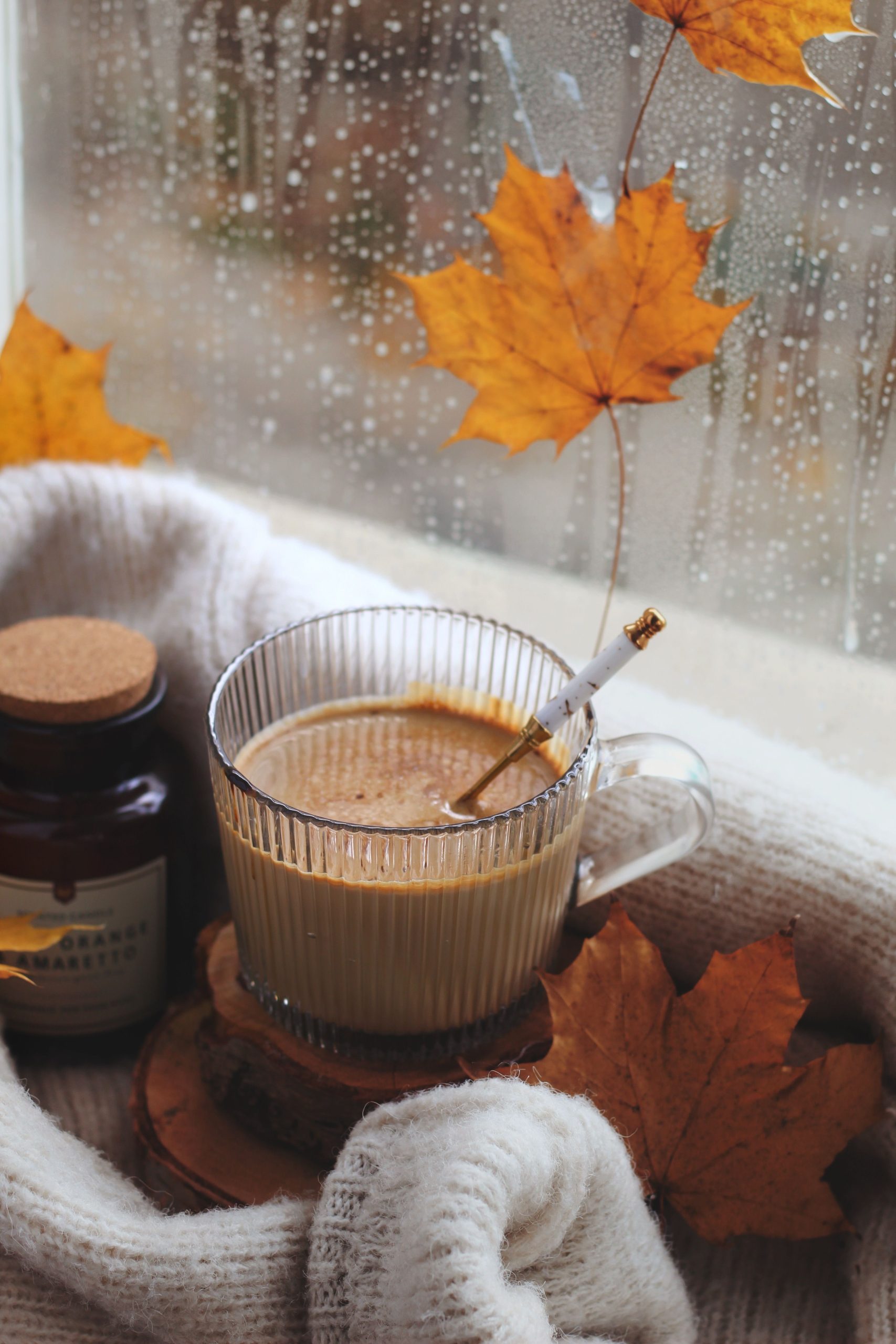 Warm coffee cup by the window with autumn leaves and sweater, setting a cozy fall mood.