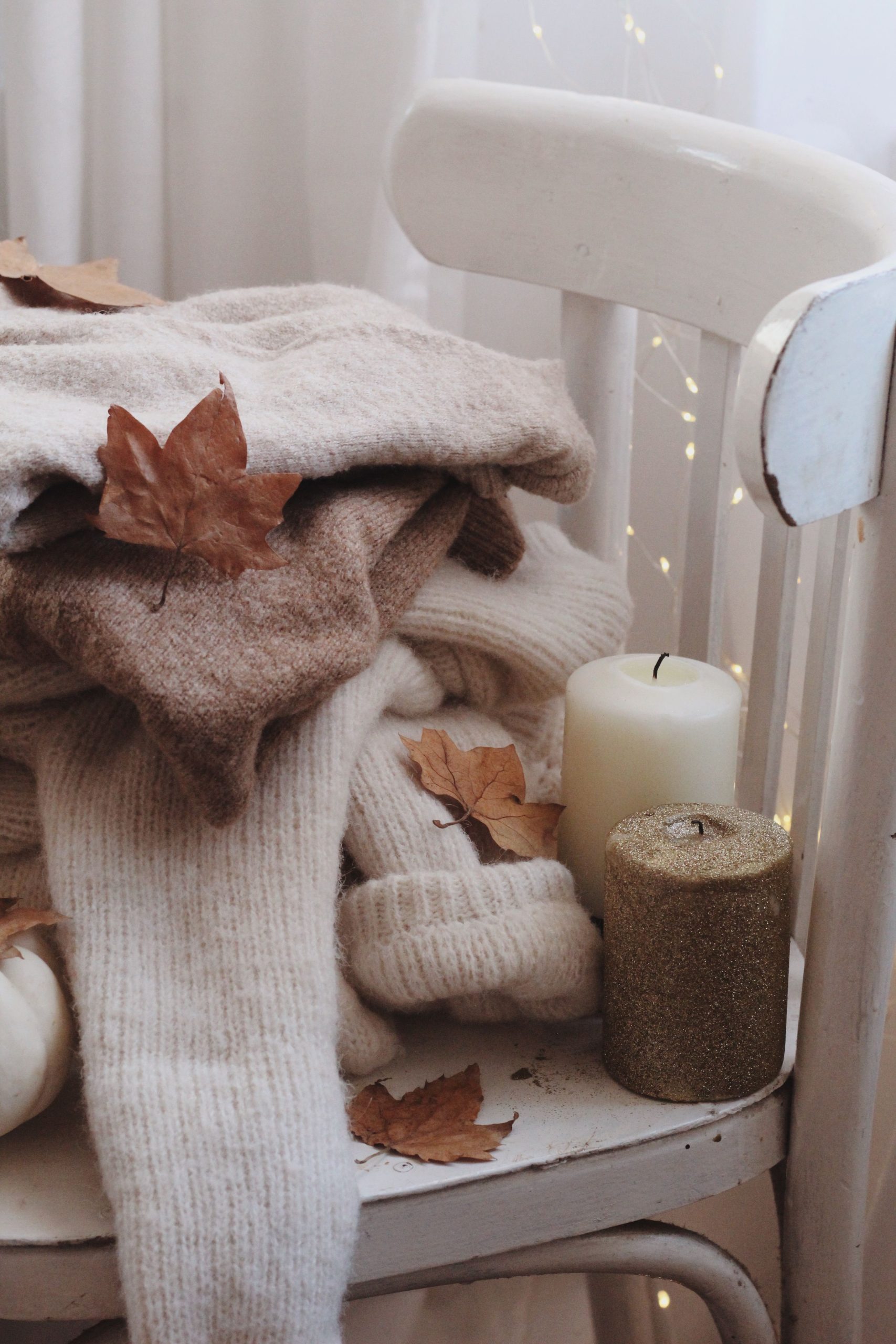 Warm fall setting with sweaters on a chair, candles, and leaves for autumn ambiance.