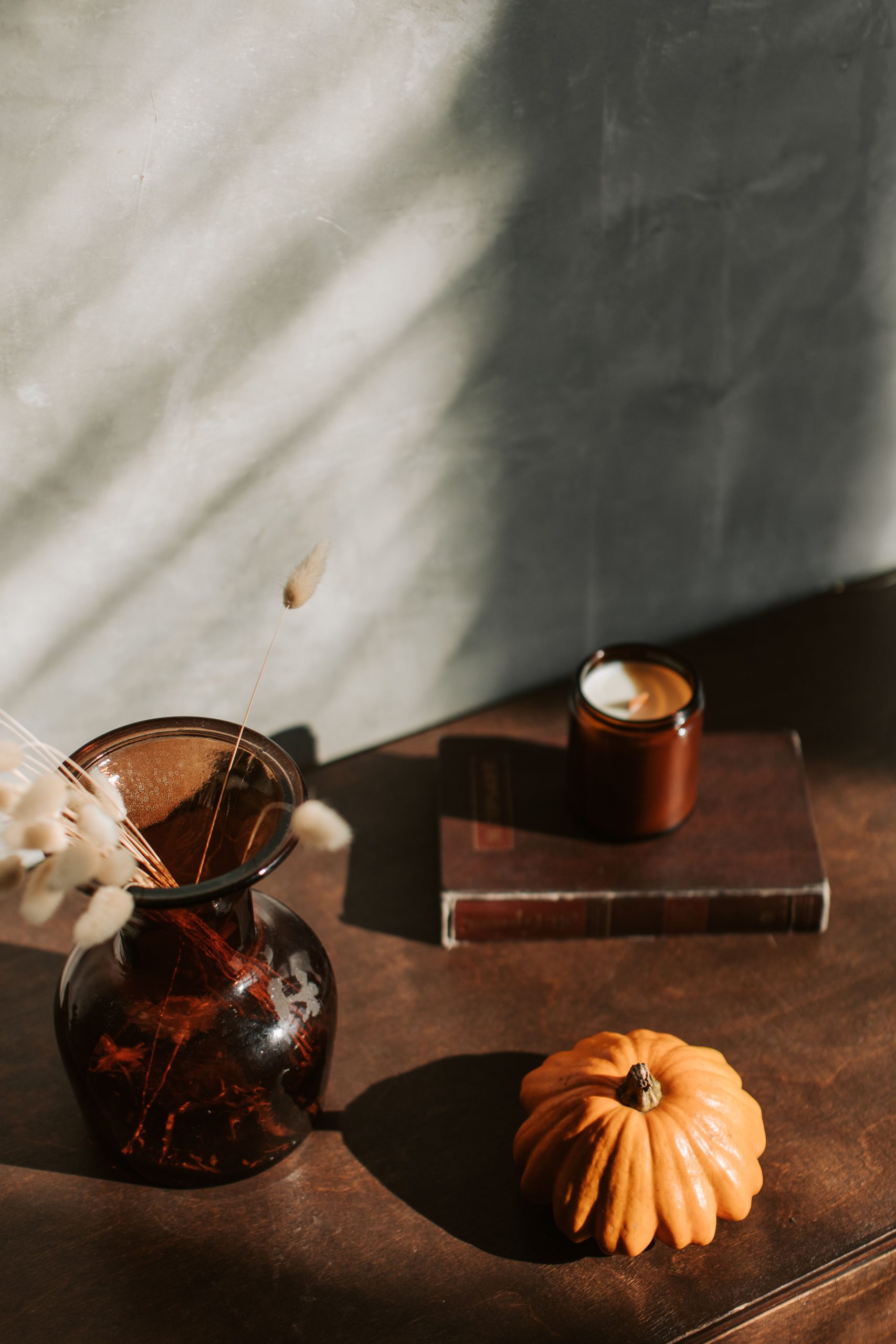 Warm still life featuring a pumpkin, candle and vase in soft light, perfect for autumn themes.