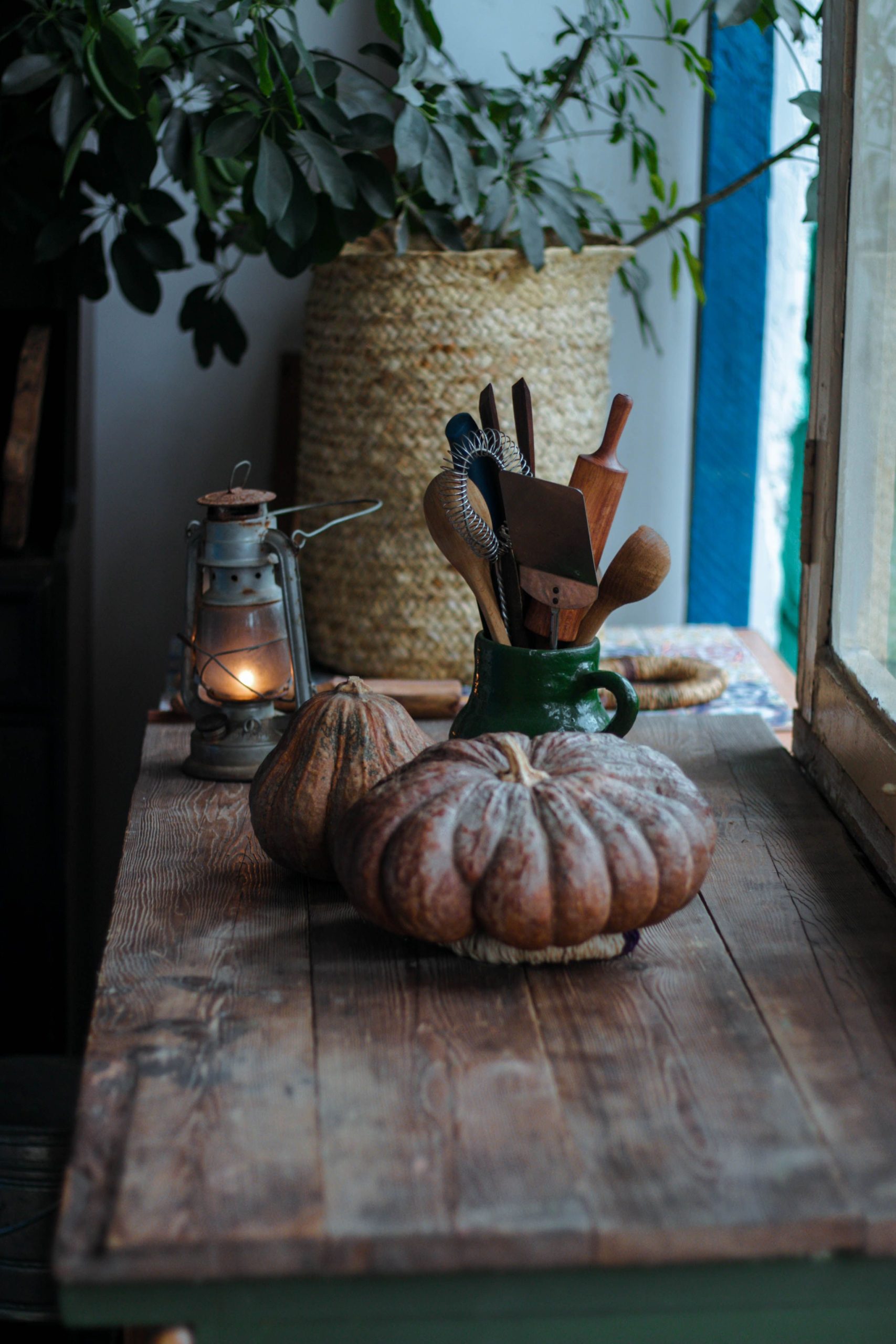 Warm wooden table with pumpkins, kitchen utensils, and a lantern, creating an autumn ambiance.