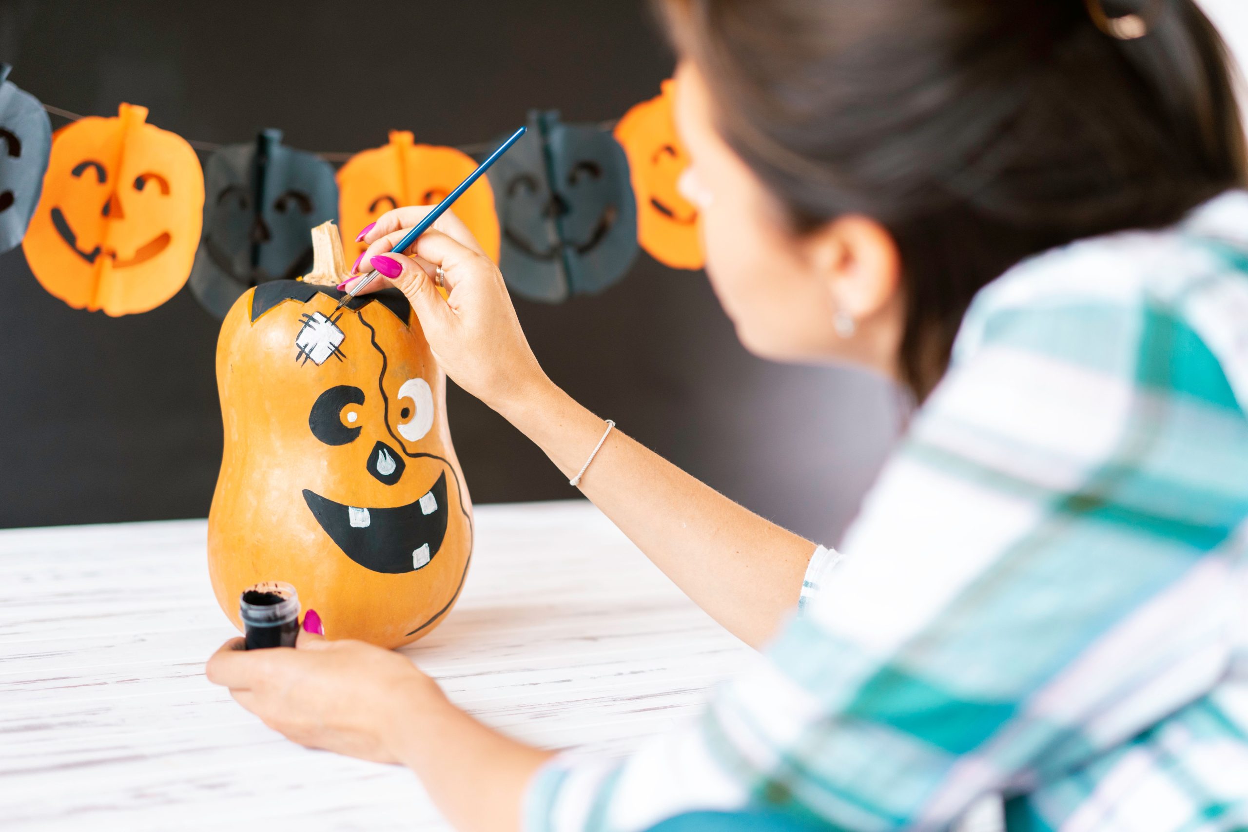 Woman painting a Halloween-themed gourd with decorations in the background.