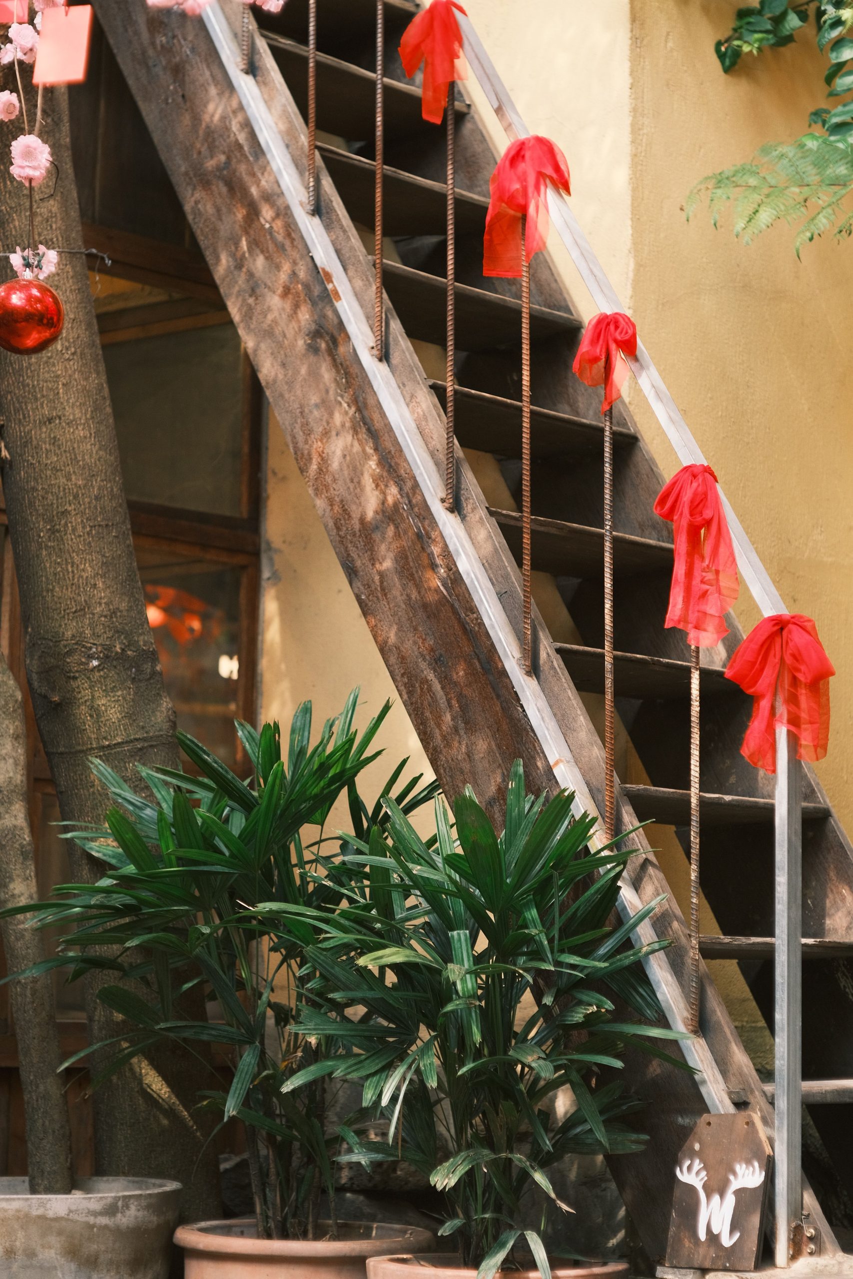 Wooden staircase adorned with red bows, surrounded by potted plants indoors.