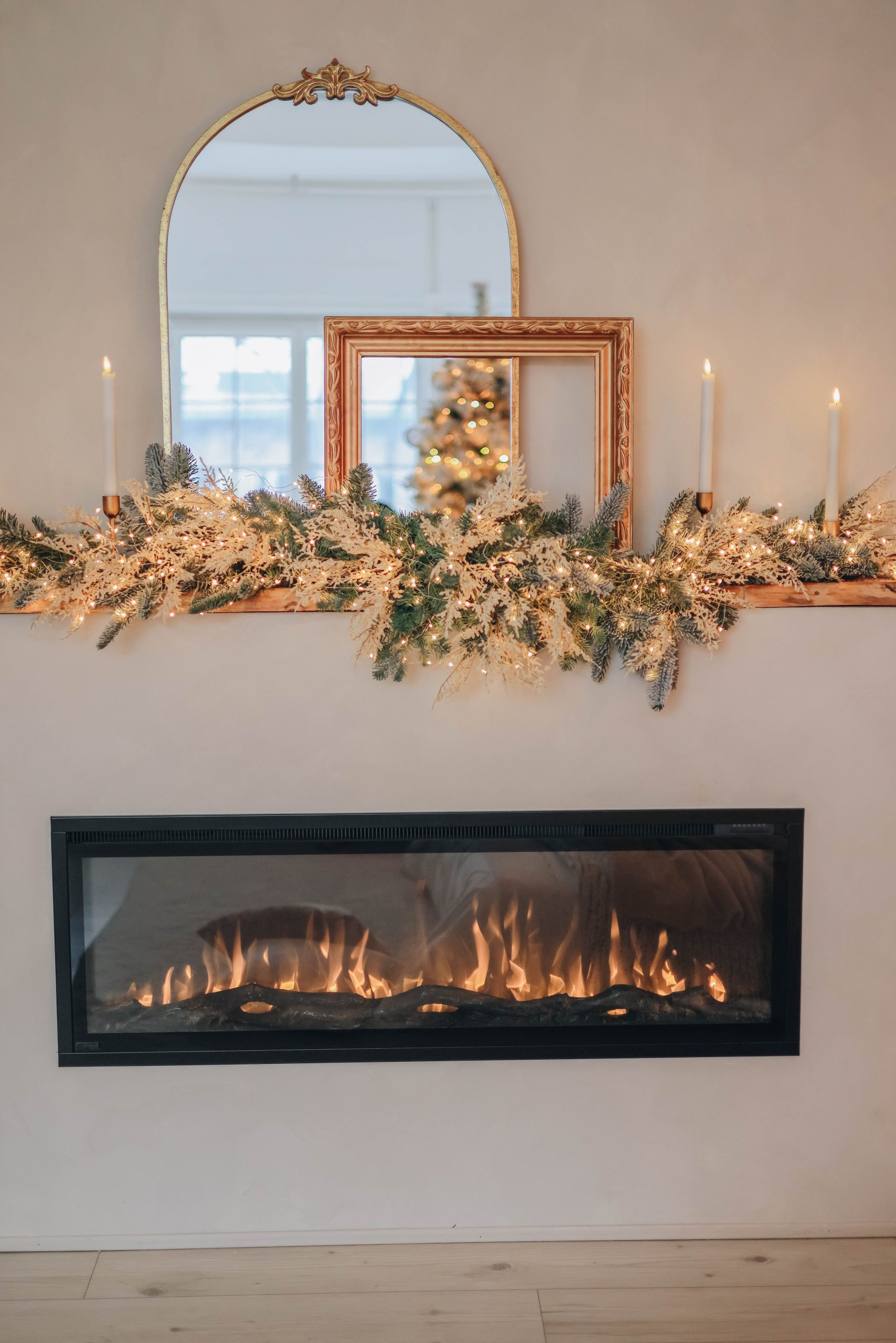 A beautifully decorated fireplace for Christmas with candles, greenery, and a festive reflection in mirrors.