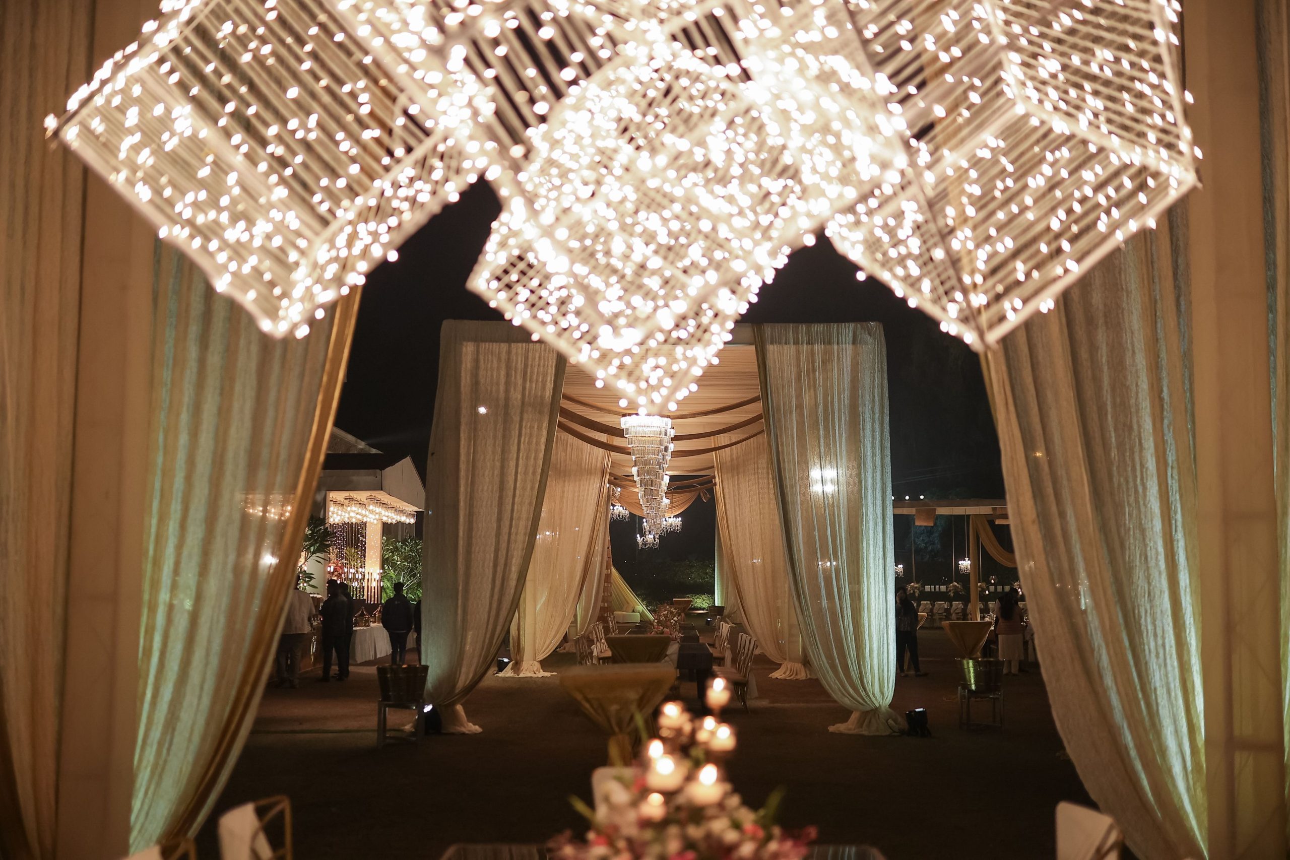 A beautifully lit outdoor event space adorned with fairy lights and draped curtains, creating a magical evening atmosphere.