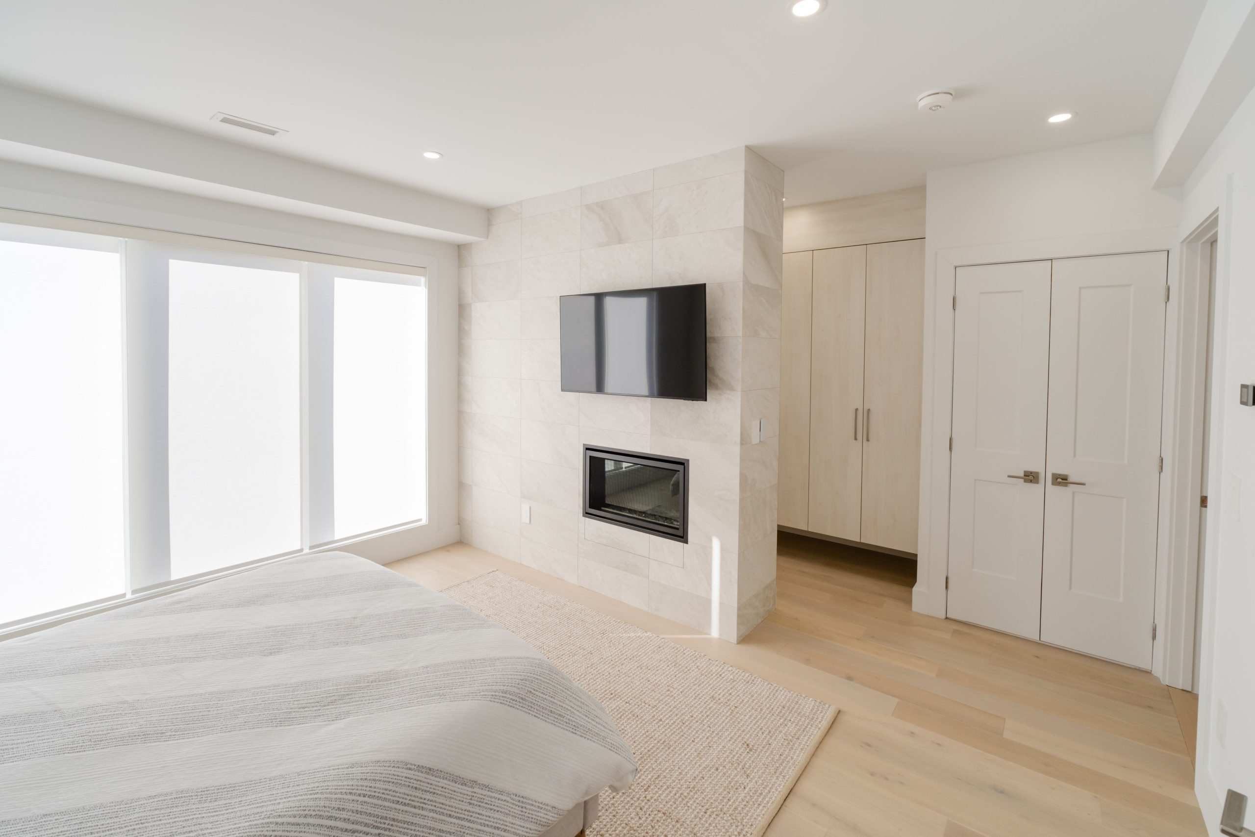 A bright, minimalist bedroom featuring a fireplace, mounted TV, and a soft color palette for a tranquil atmosphere.