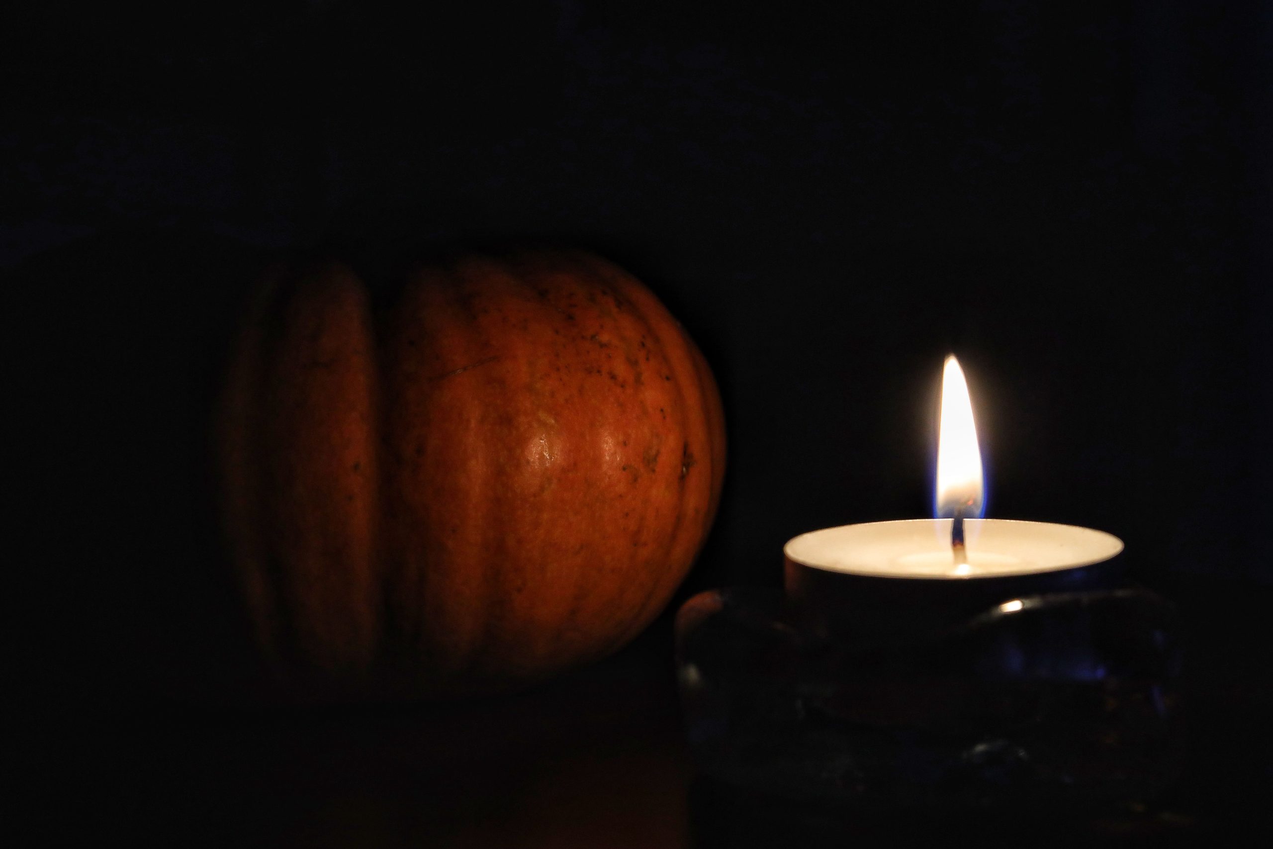 A candle illuminates a pumpkin in a dark, warm autumn setting.