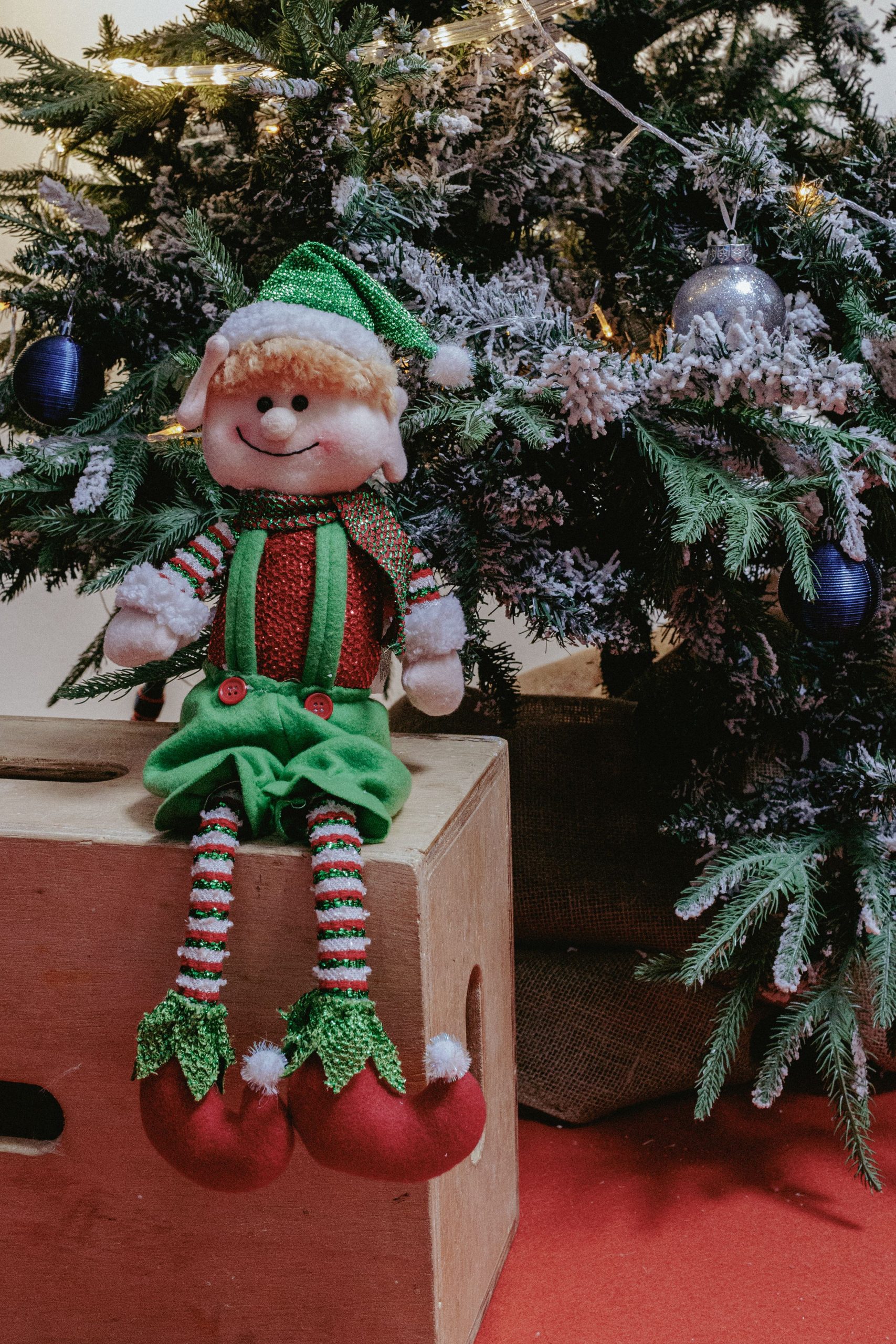 A cheerful elf doll next to a Christmas tree with ornaments in São Paulo.