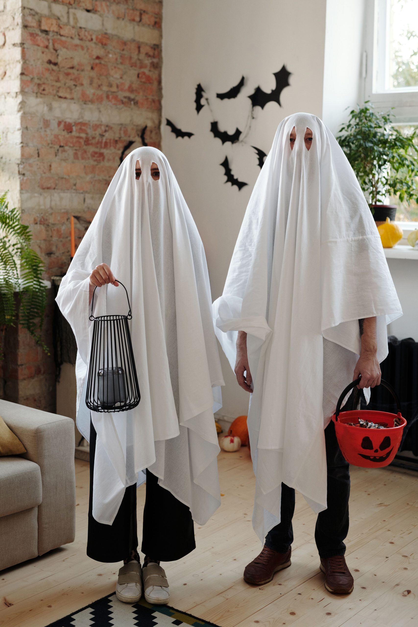 A couple in ghost costumes celebrating Halloween indoors with decorations.