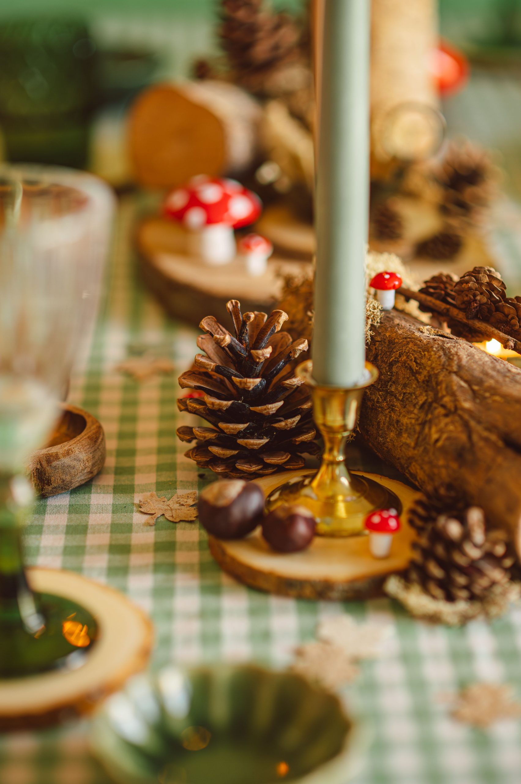 A cozy fall table setting with pinecones, mushrooms, and a candle on a checkered cloth.