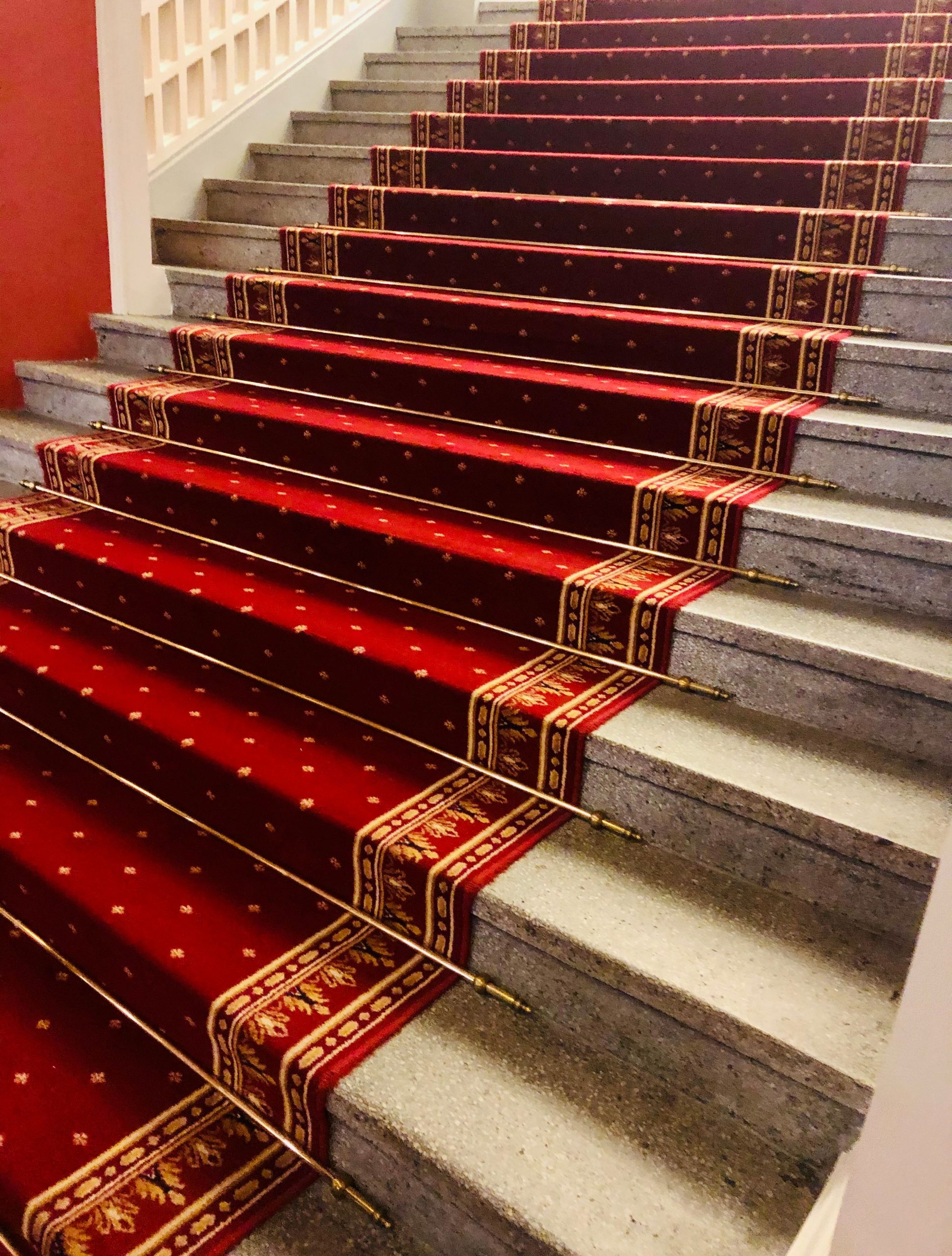 A luxurious staircase adorned with a rich, red carpet featuring intricate golden patterns.