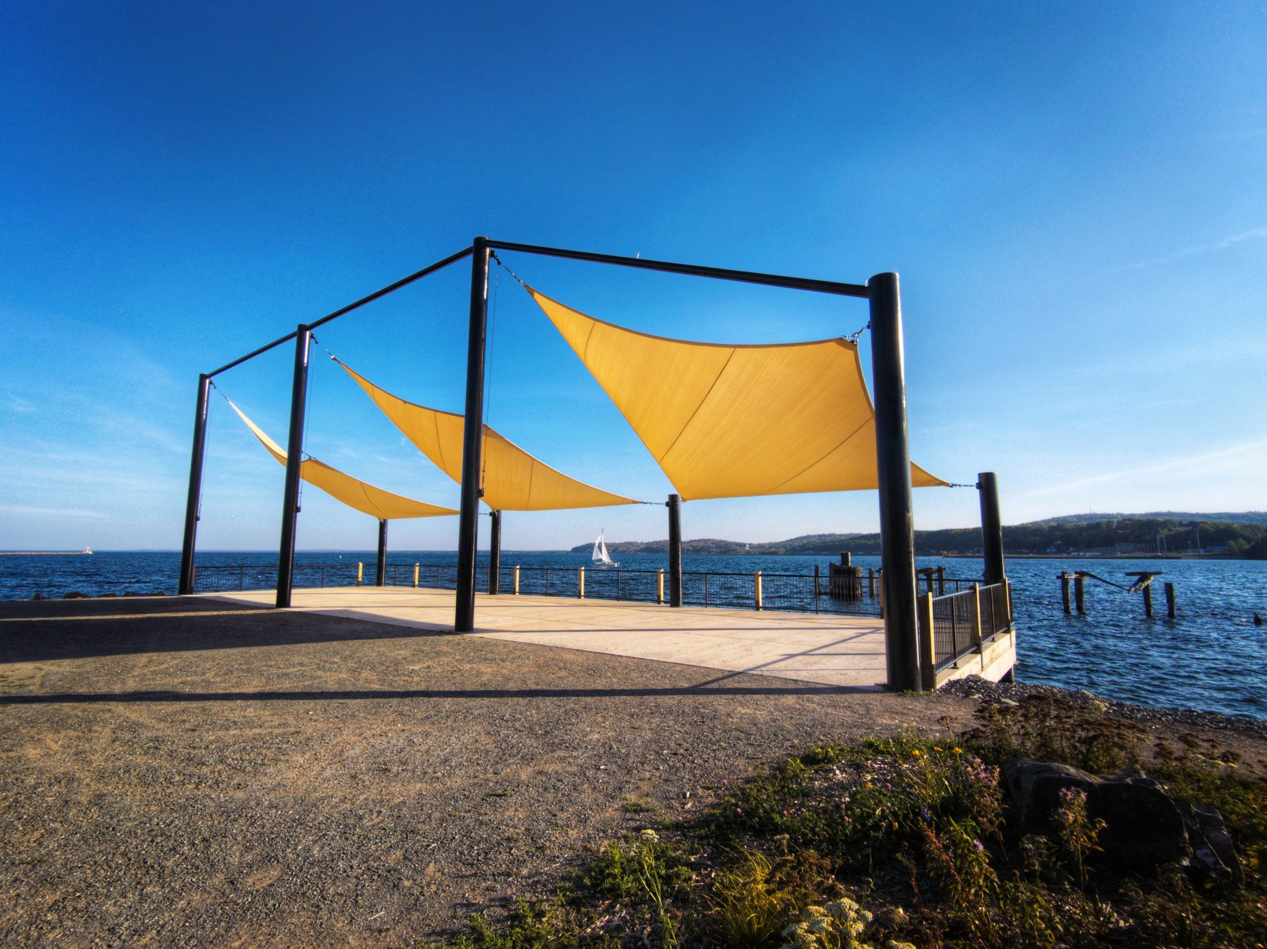 A modern outdoor terrace with yellow sunshades by the scenic coast under a clear blue sky.
