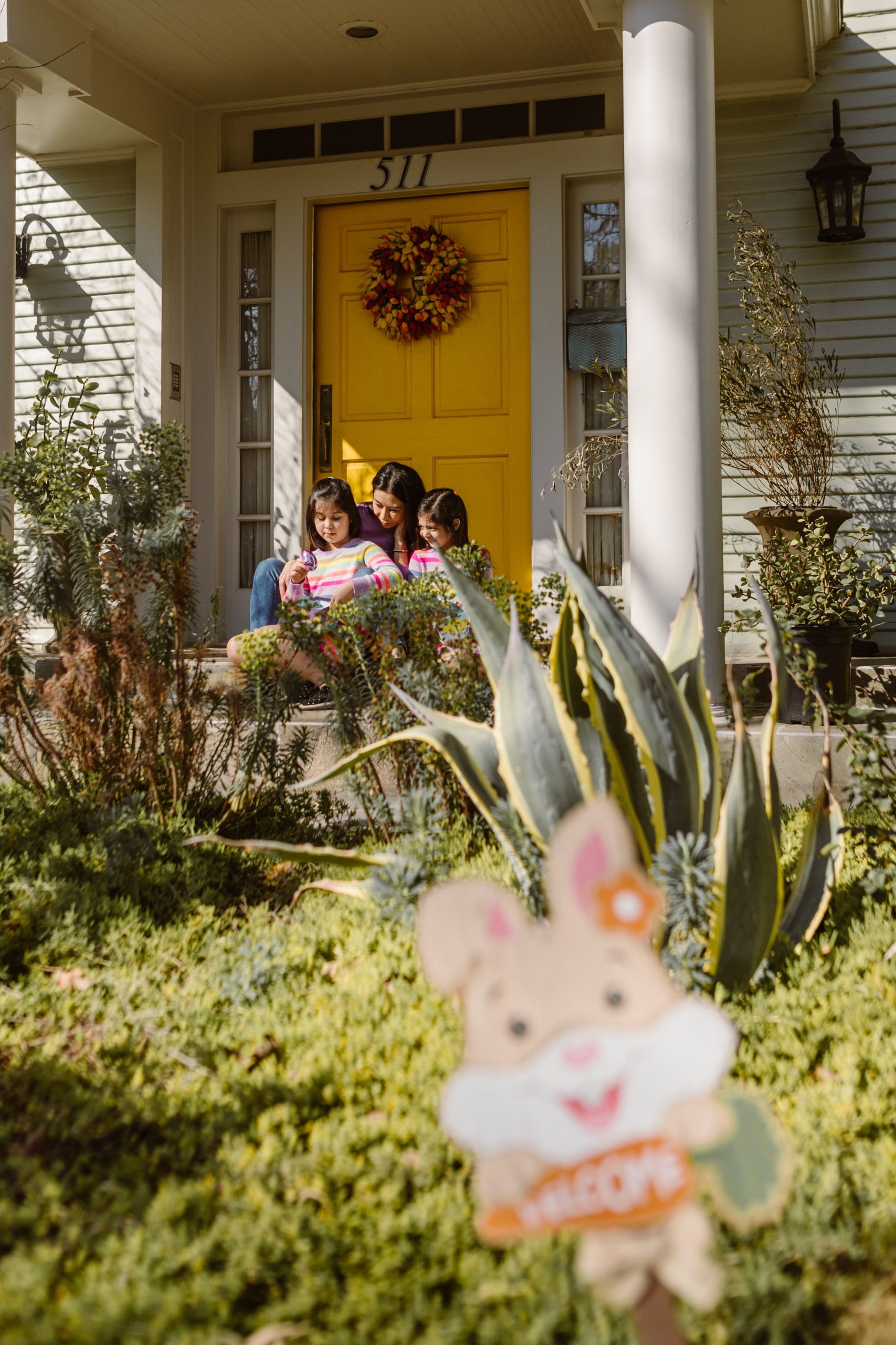 A mother and her daughters enjoy Easter together on their porch, featuring a vibrant yellow door.