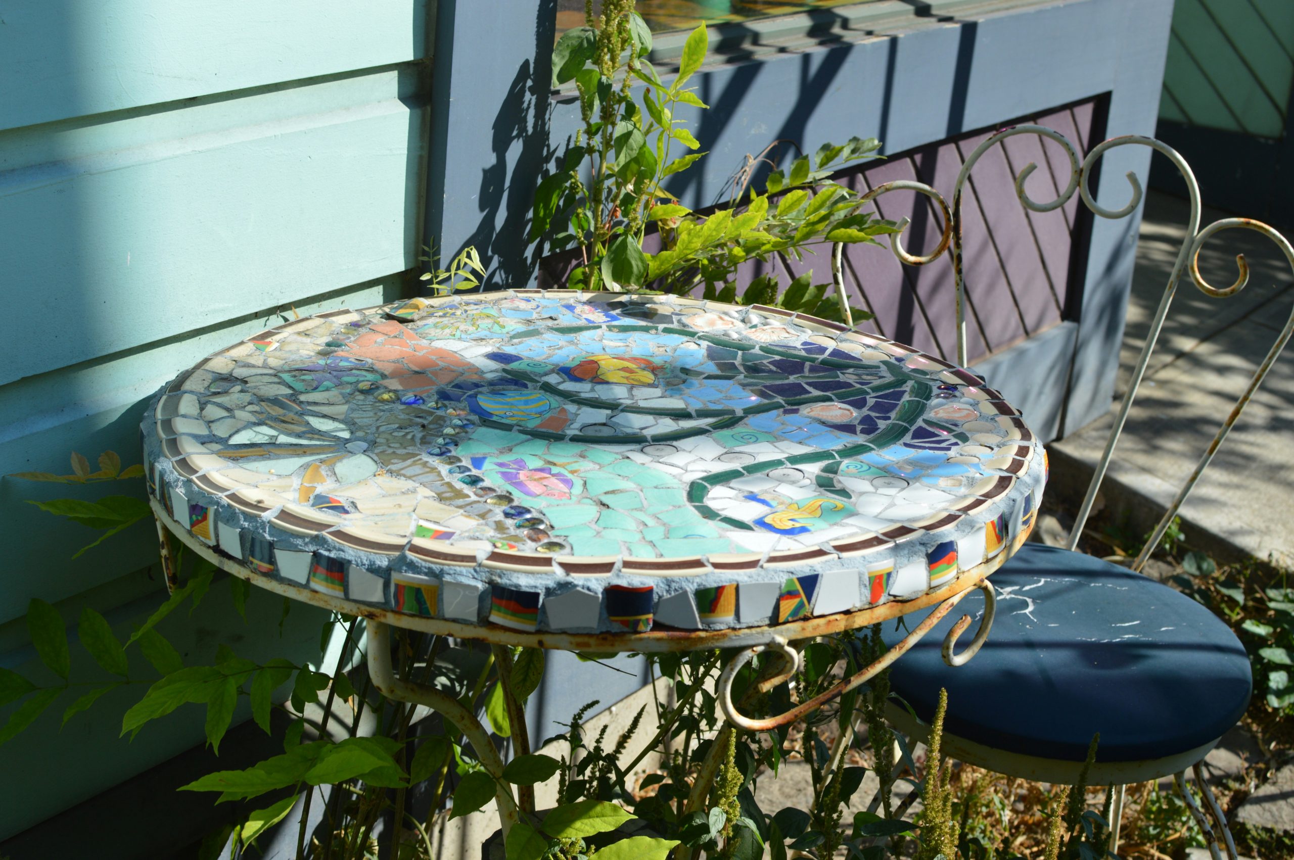 A round mosaic table with colorful tile patterns beside a metal chair