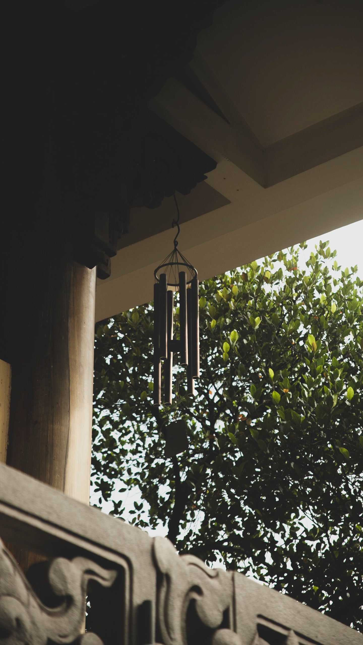 A serene wind chime hangs in a garden setting, capturing light and leafy shadows.