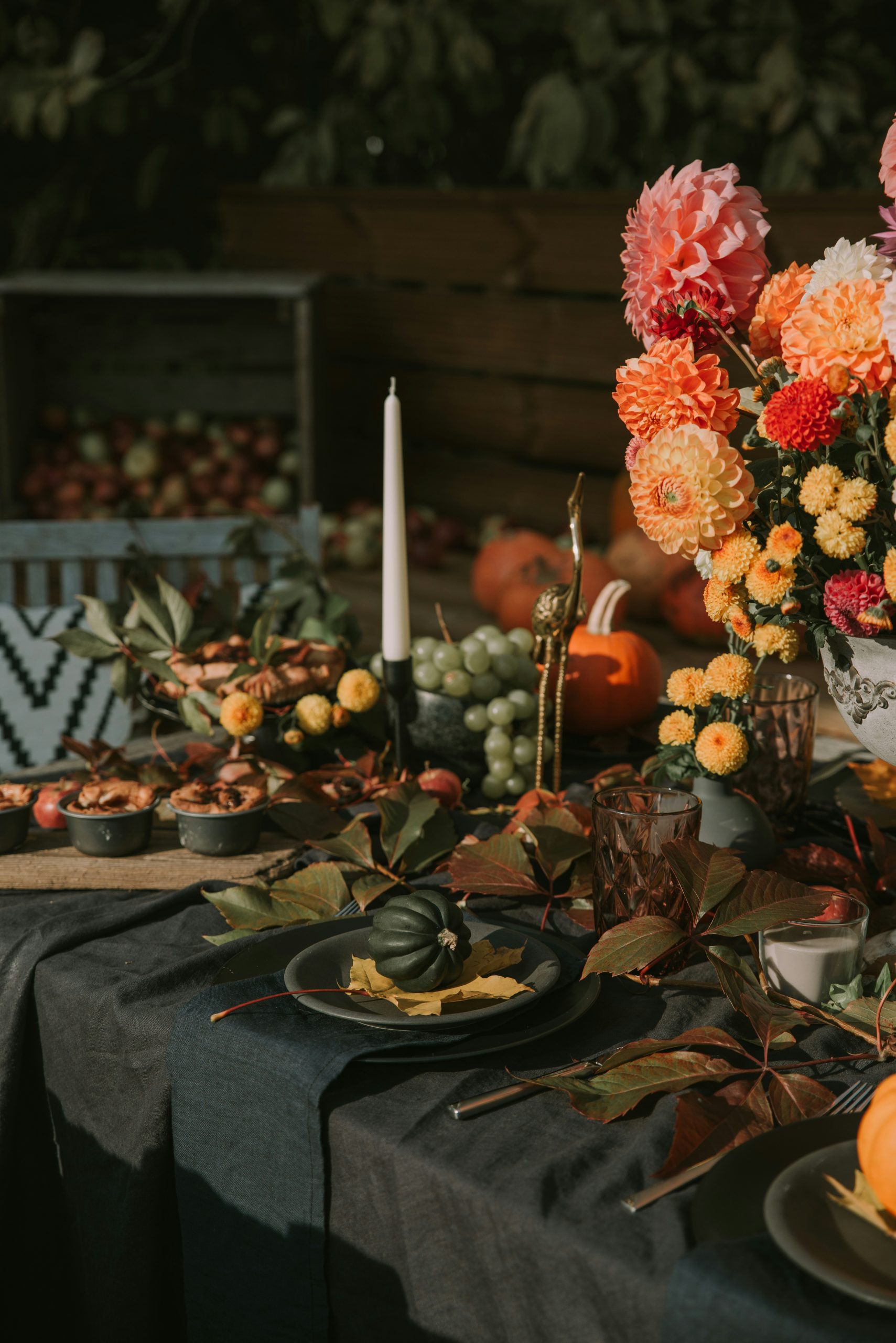 A table set for autumn with dahlias, pumpkins, grapes, and small pies