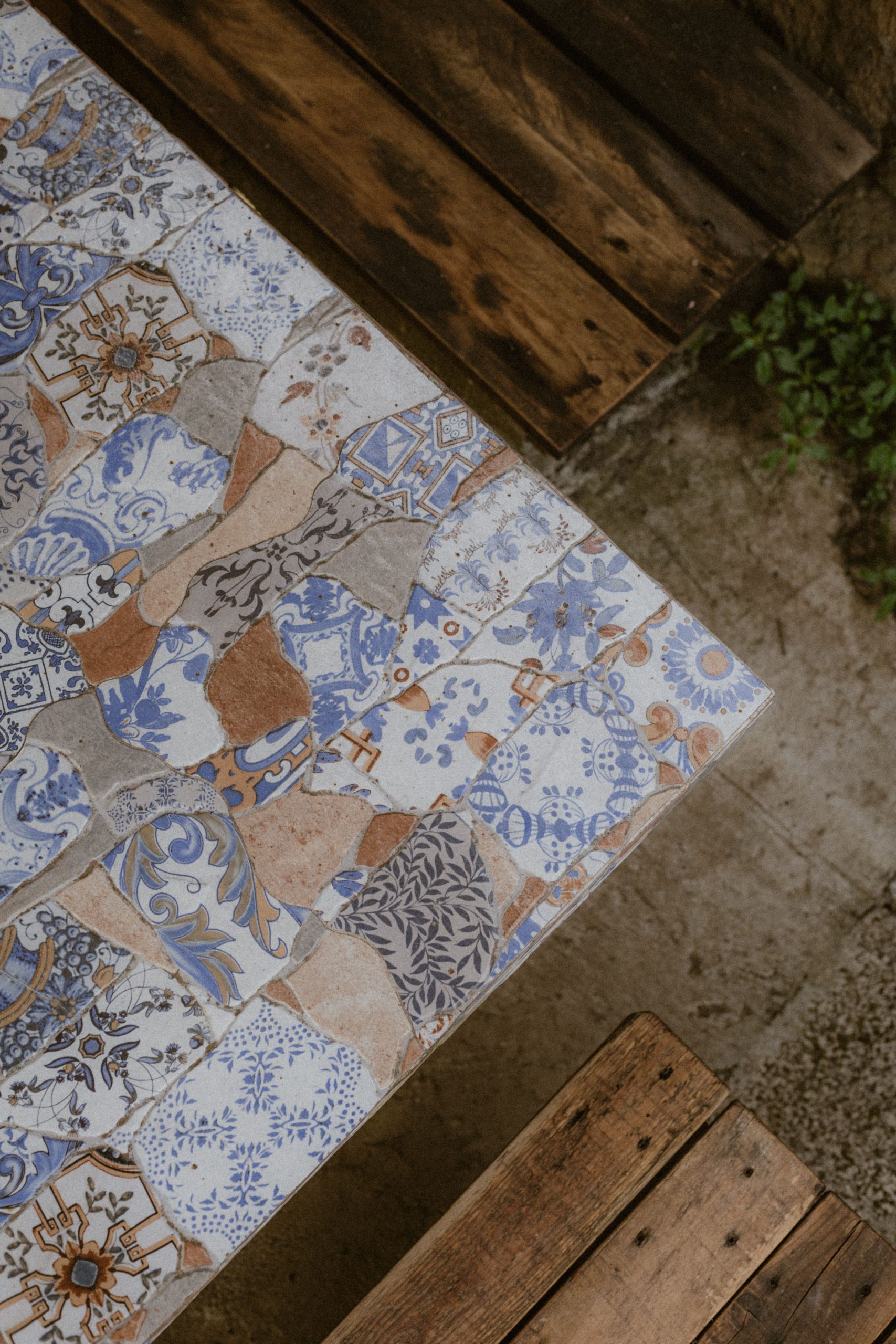 A top view of a mosaic tiled table with wooden benches, showcasing intricate patterns in a rustic outdoor setting.