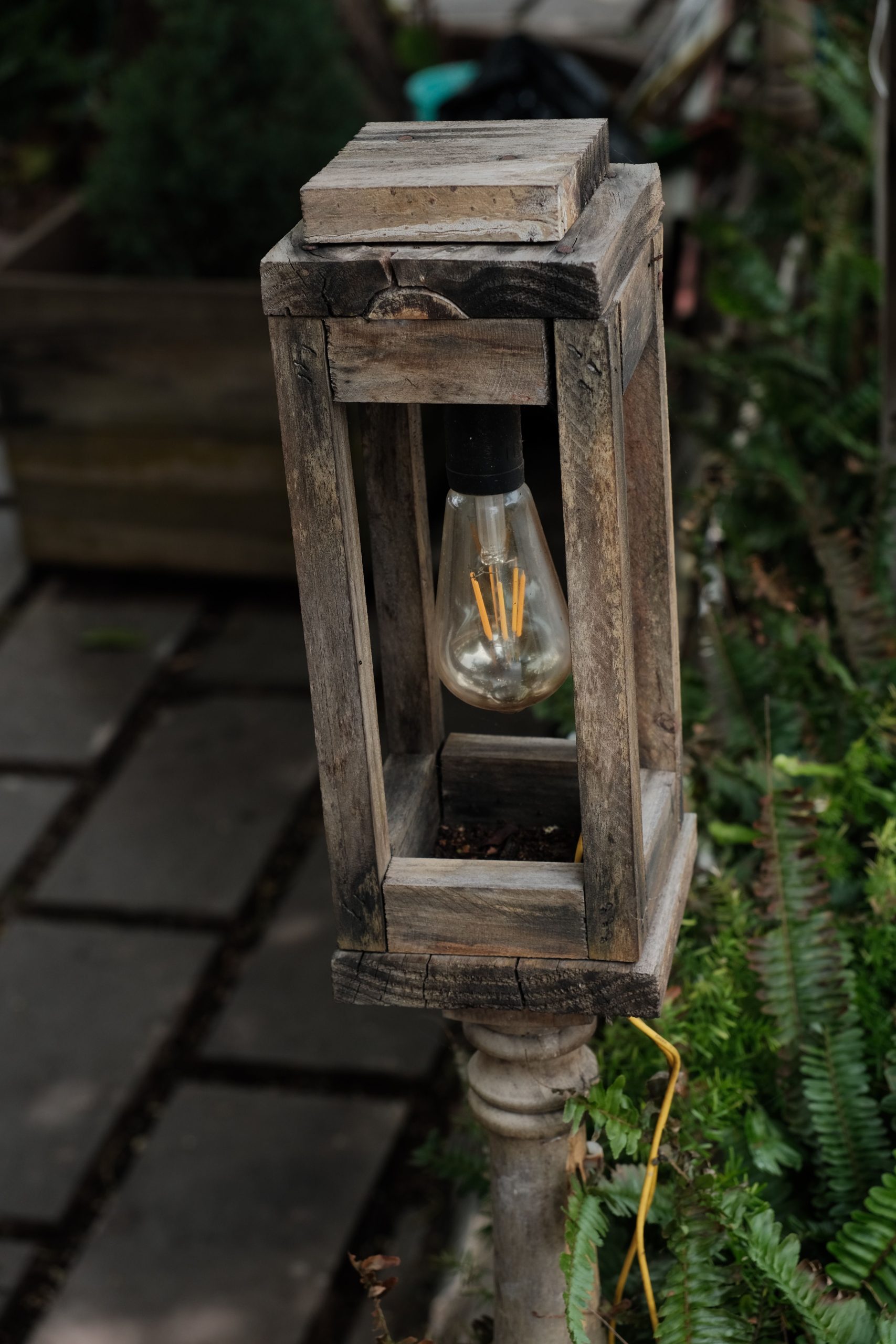 A vintage wooden lantern with an Edison bulb in an outdoor garden.