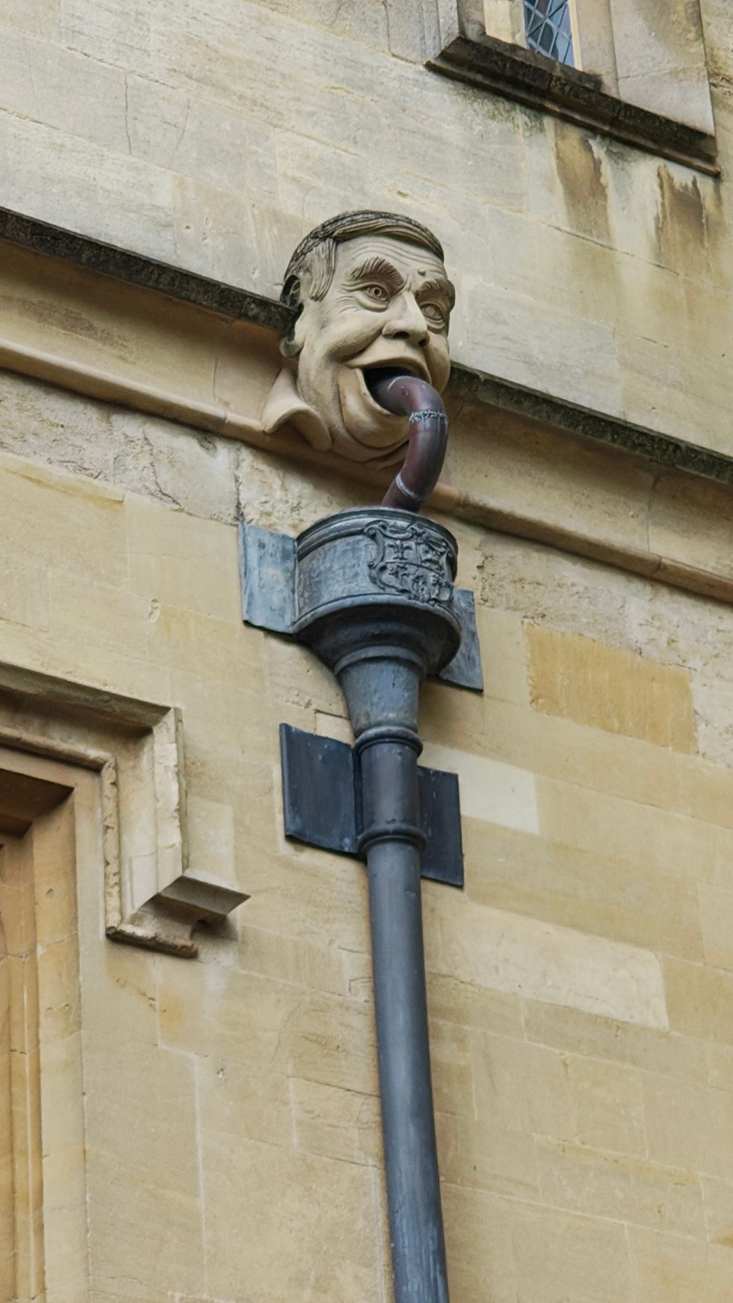 A whimsical gargoyle face decorates an old building's rainwater downspout.