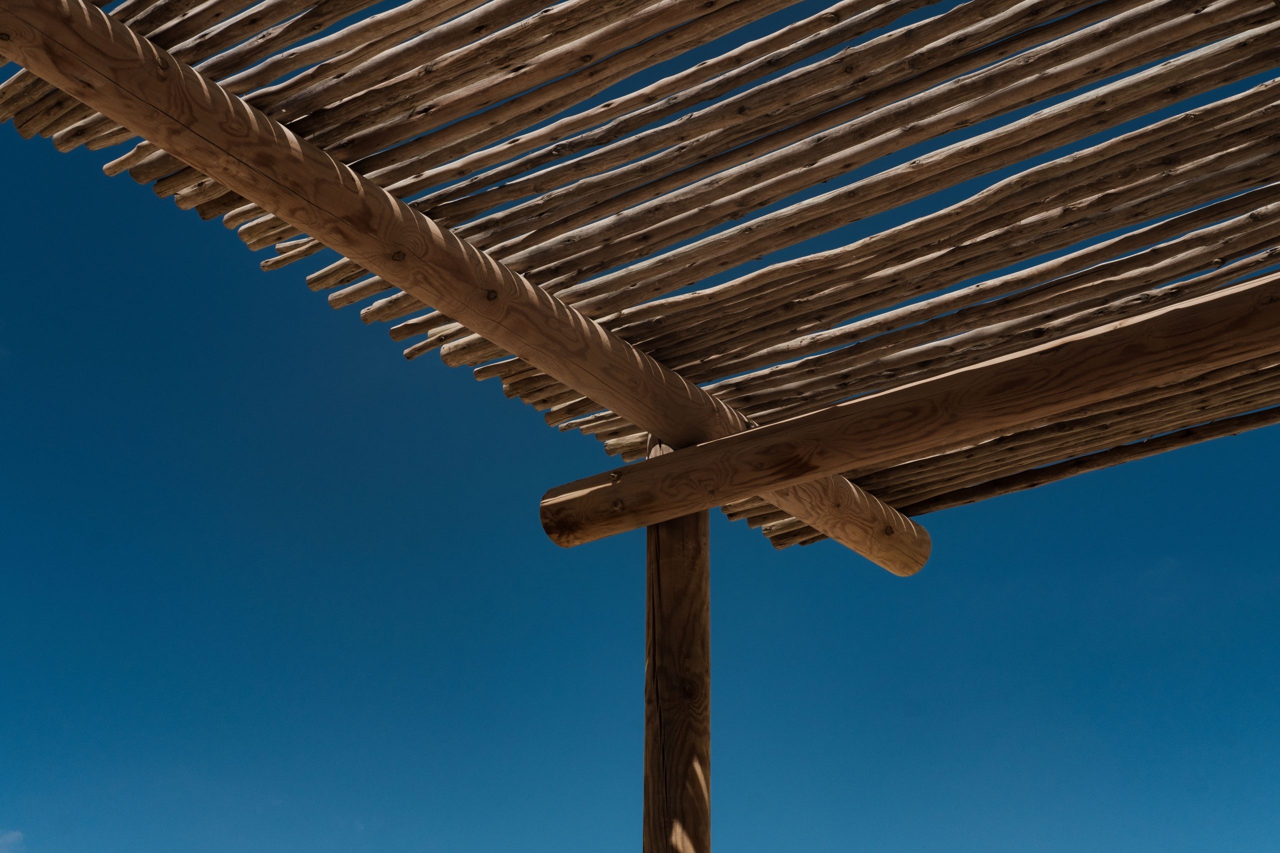An artistic perspective of a wooden pergola with a deep blue sky backdrop, showcasing natural materials.