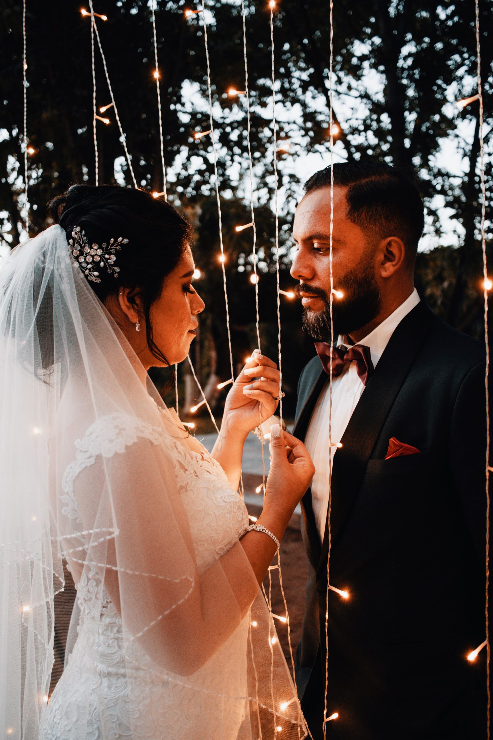 Beautiful bride and groom sharing a tender moment under glowing string lights outdoors.