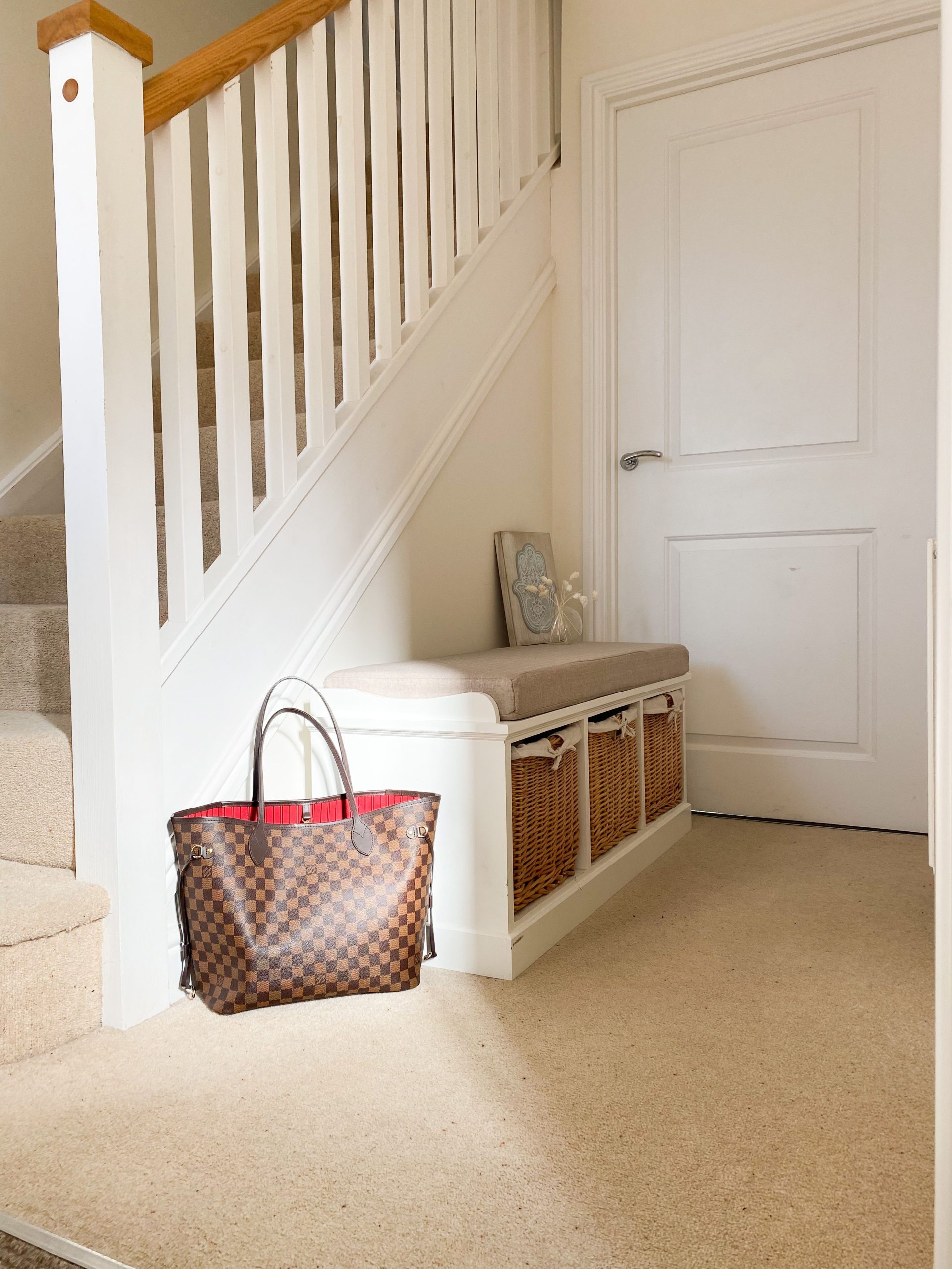 Bright entryway featuring a stylish storage bench with wicker baskets and an elegant handbag.