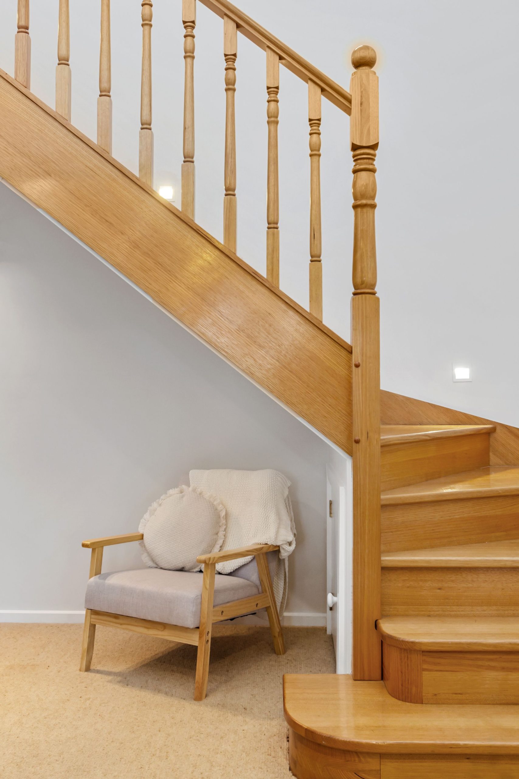 Bright indoor scene with a wooden staircase and a cozy chair underneath.