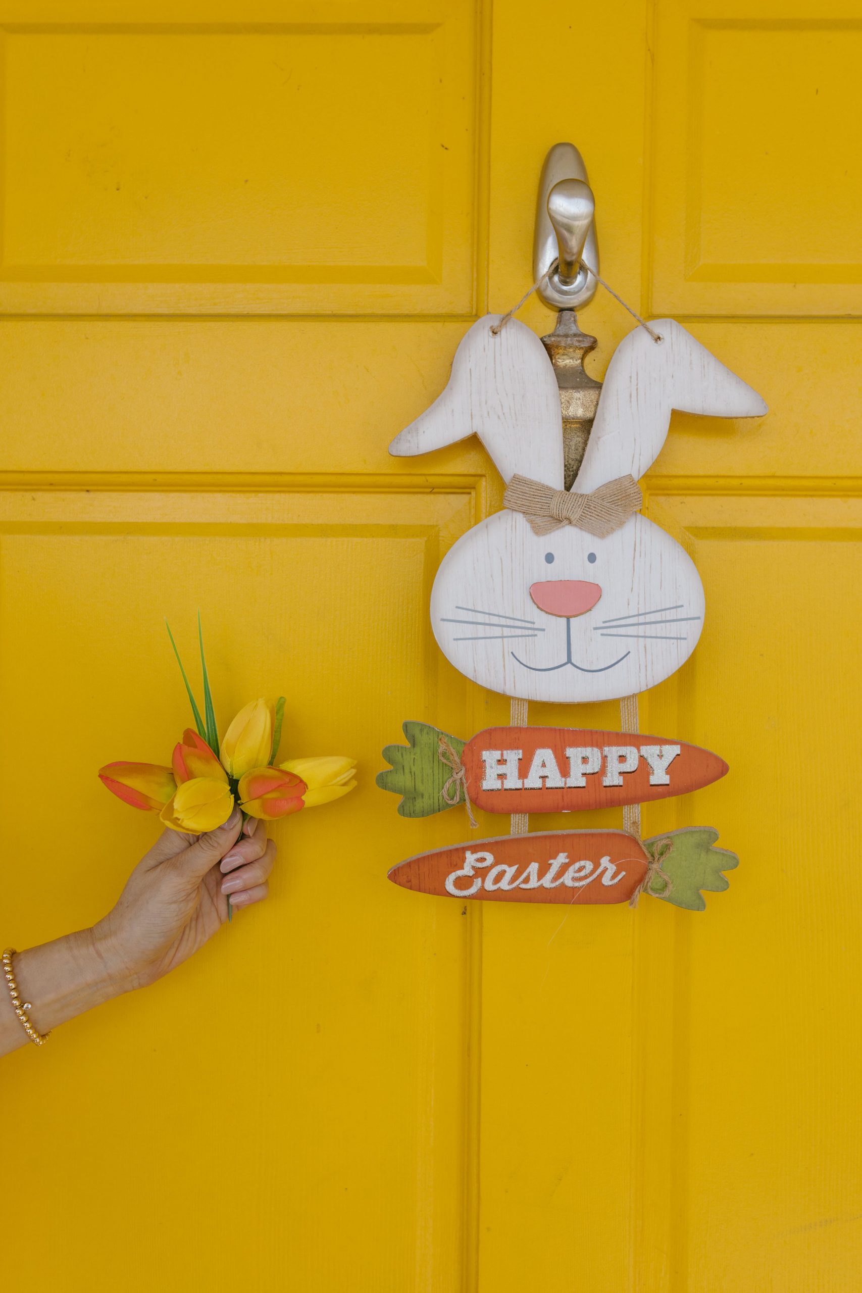 Charming Easter bunny decoration on a vibrant yellow door with a hand holding flowers.