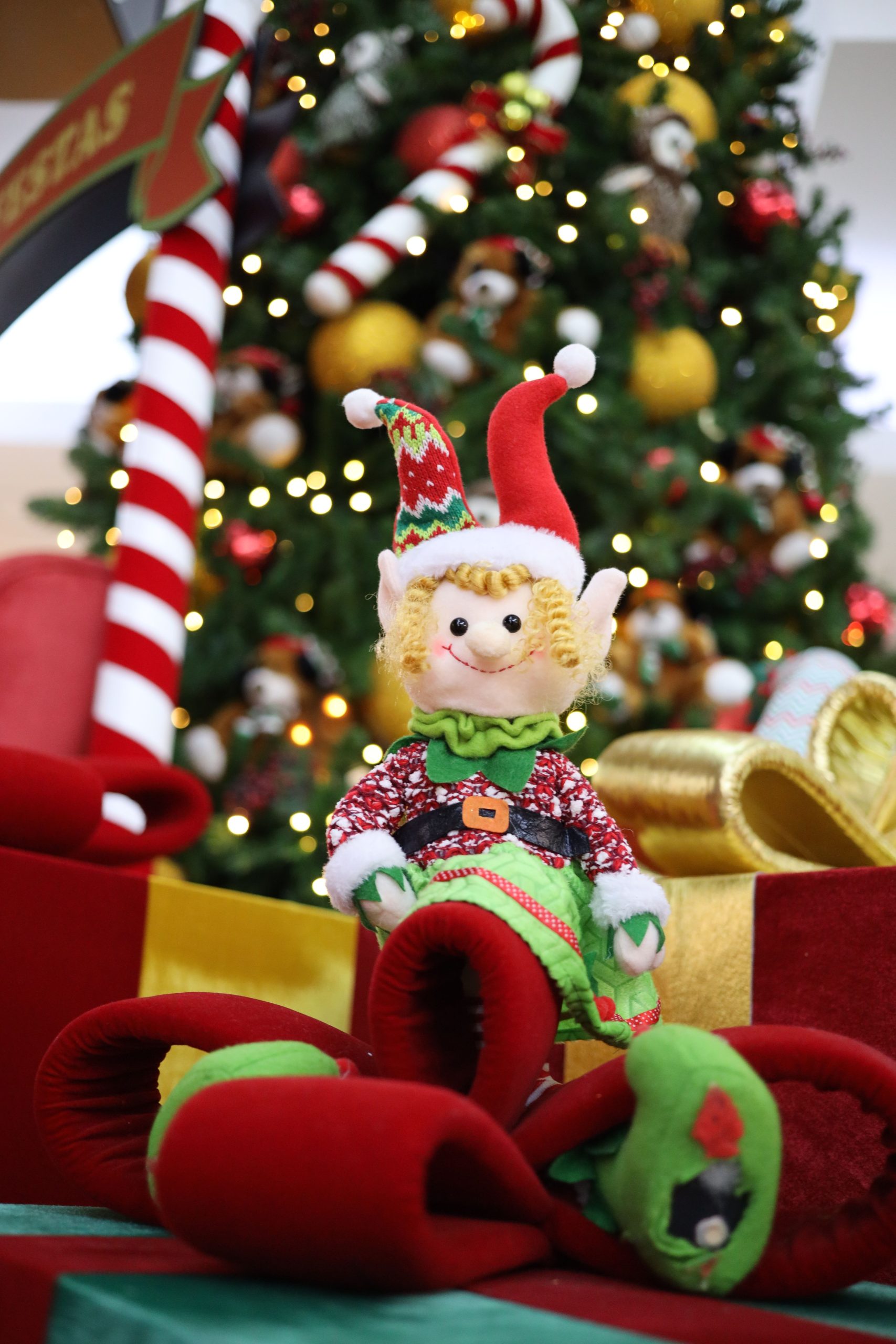 Charming elf doll in front of a decorated Christmas tree, evoking holiday cheer.