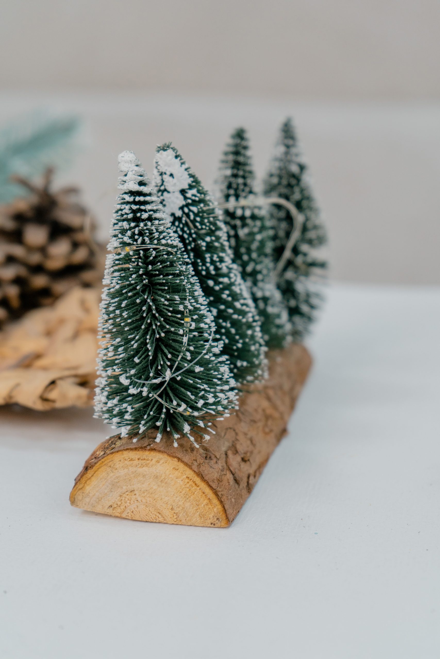 Charming miniature pine tree decoration on wood log with faux snow, perfect for winter decor.