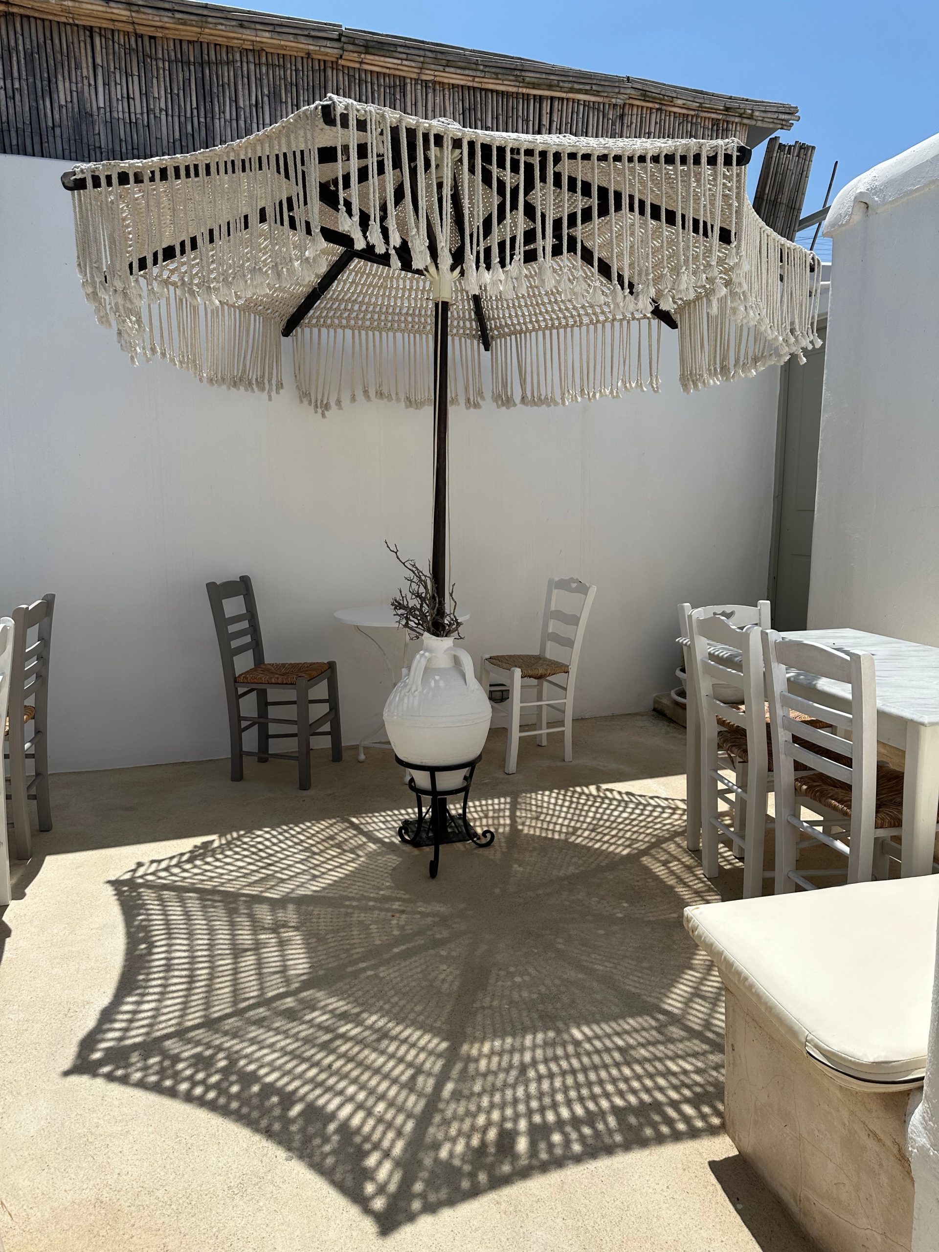 Chic outdoor restaurant patio with macrame sunshade and rustic chairs, perfect for summer dining.
