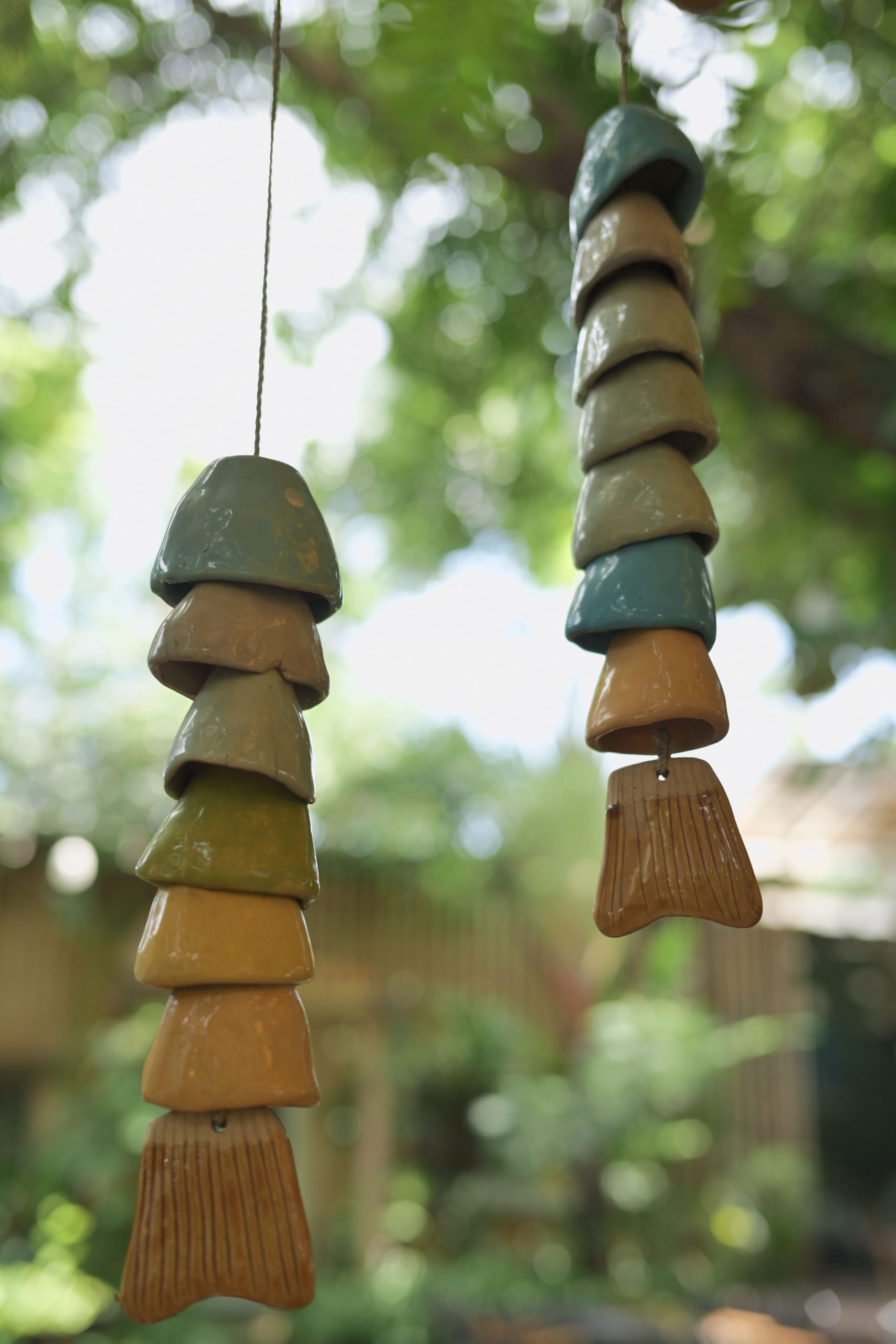 Close-up of ceramic wind chimes hanging in a sunlit garden, showcasing earthy tones and a peaceful ambiance.