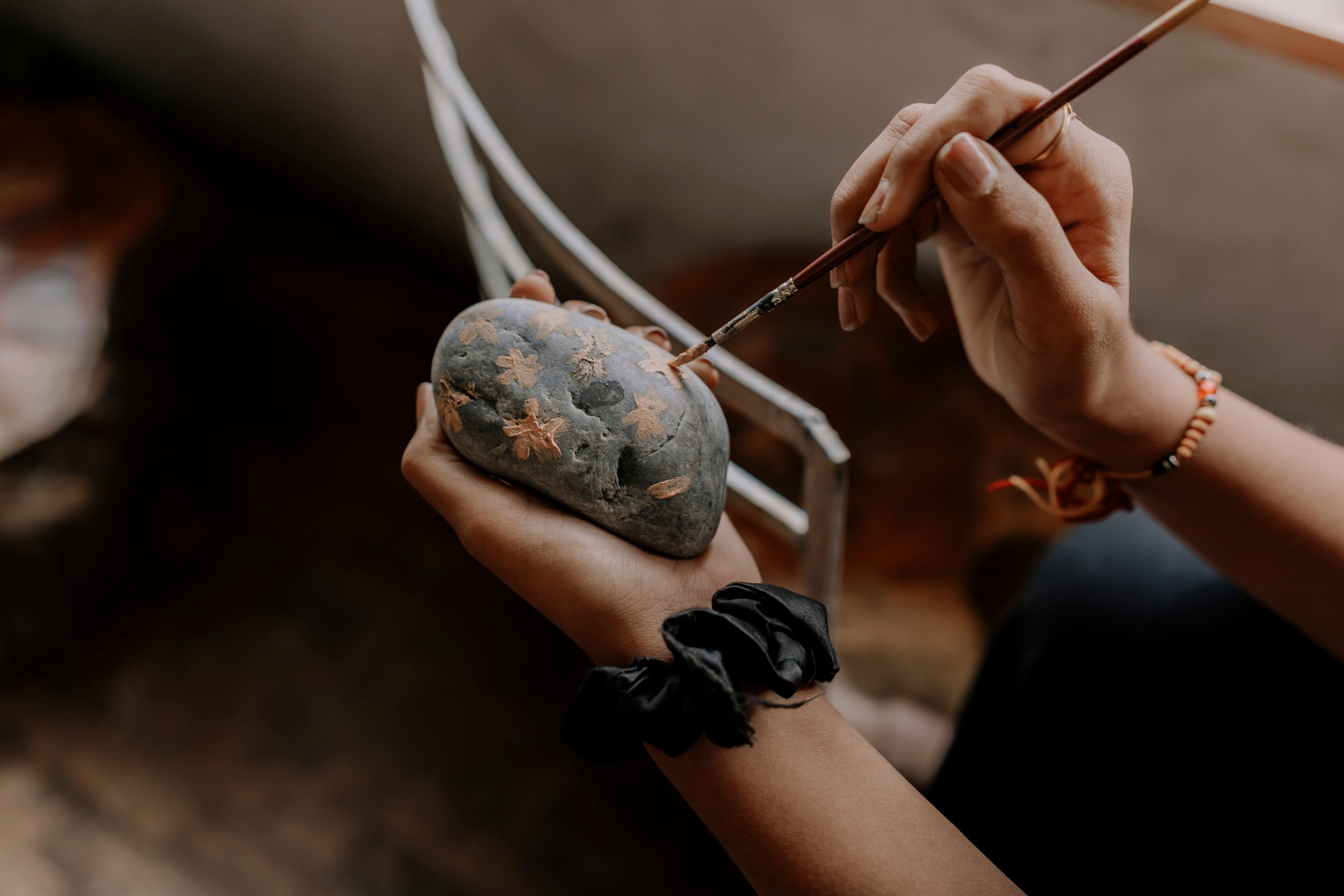 Close-up of hands painting intricate designs on a stone, showcasing artistic creativity indoors.