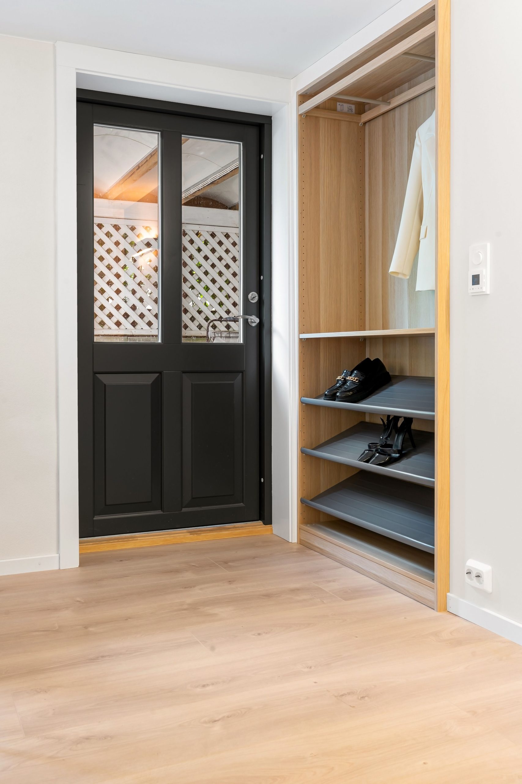 Contemporary home entrance featuring a black door and organized shoe closet with wooden flooring.
