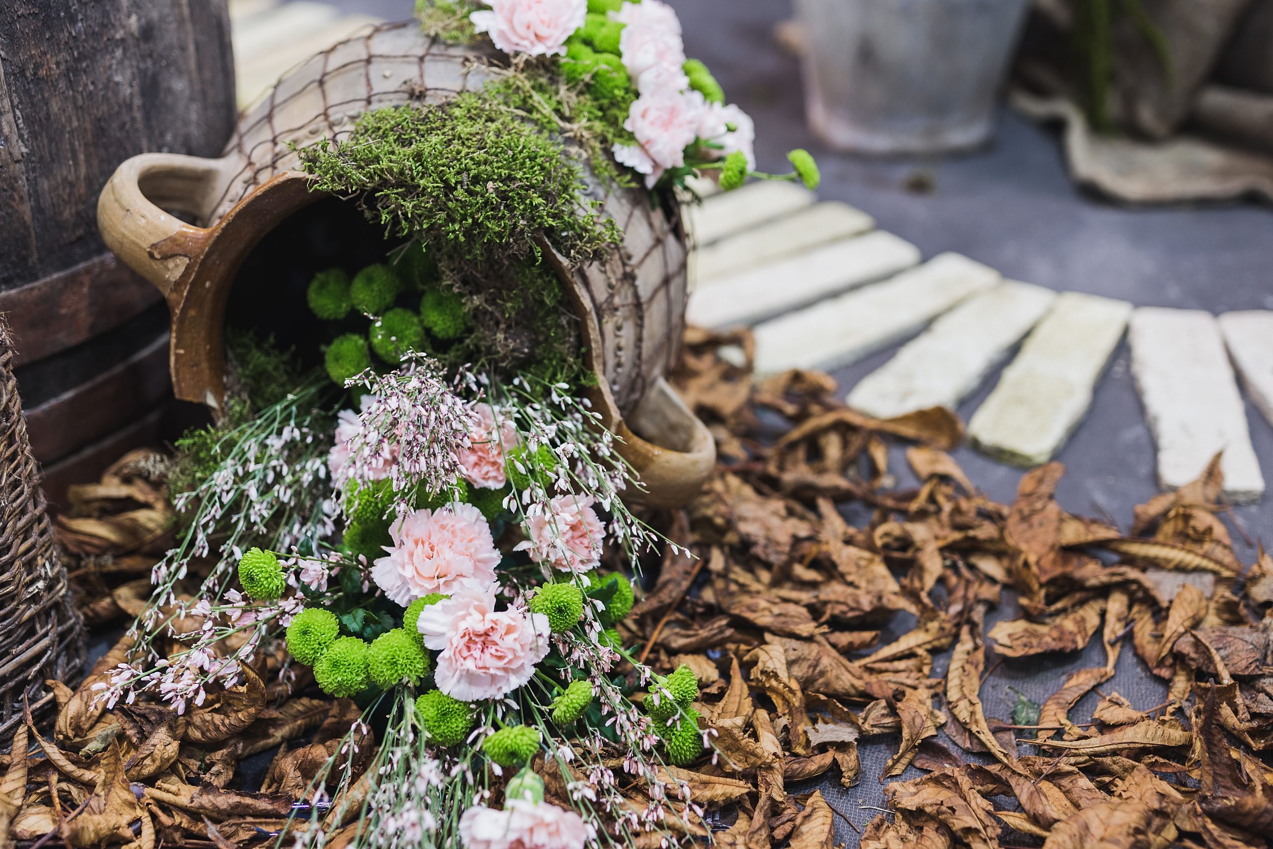 Creative floral arrangement in a rustic setting with fresh pink carnations and green accents spilling from a clay pot.