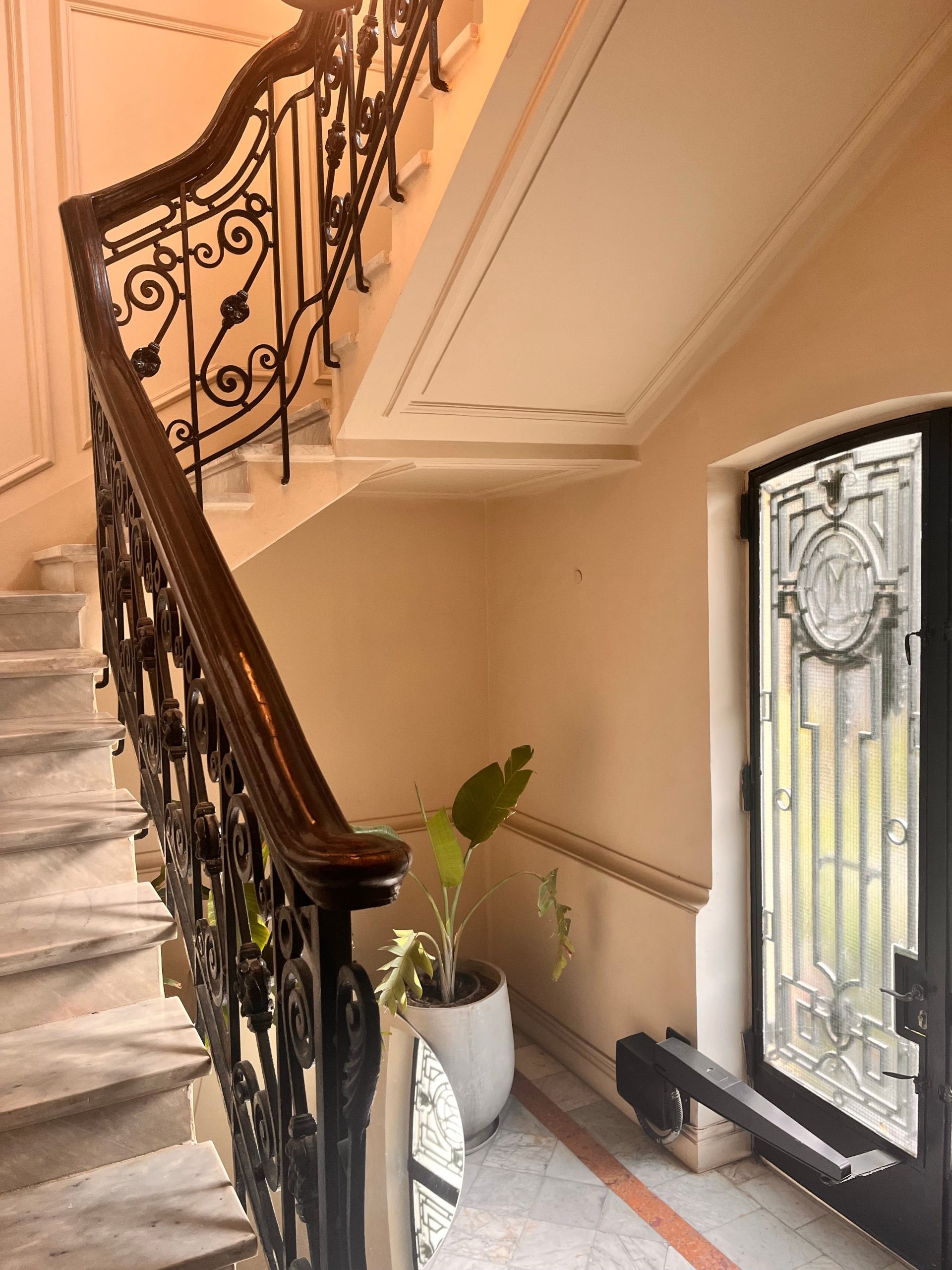 Elegant indoor stairwell with ornate iron railings and decorative glass door.